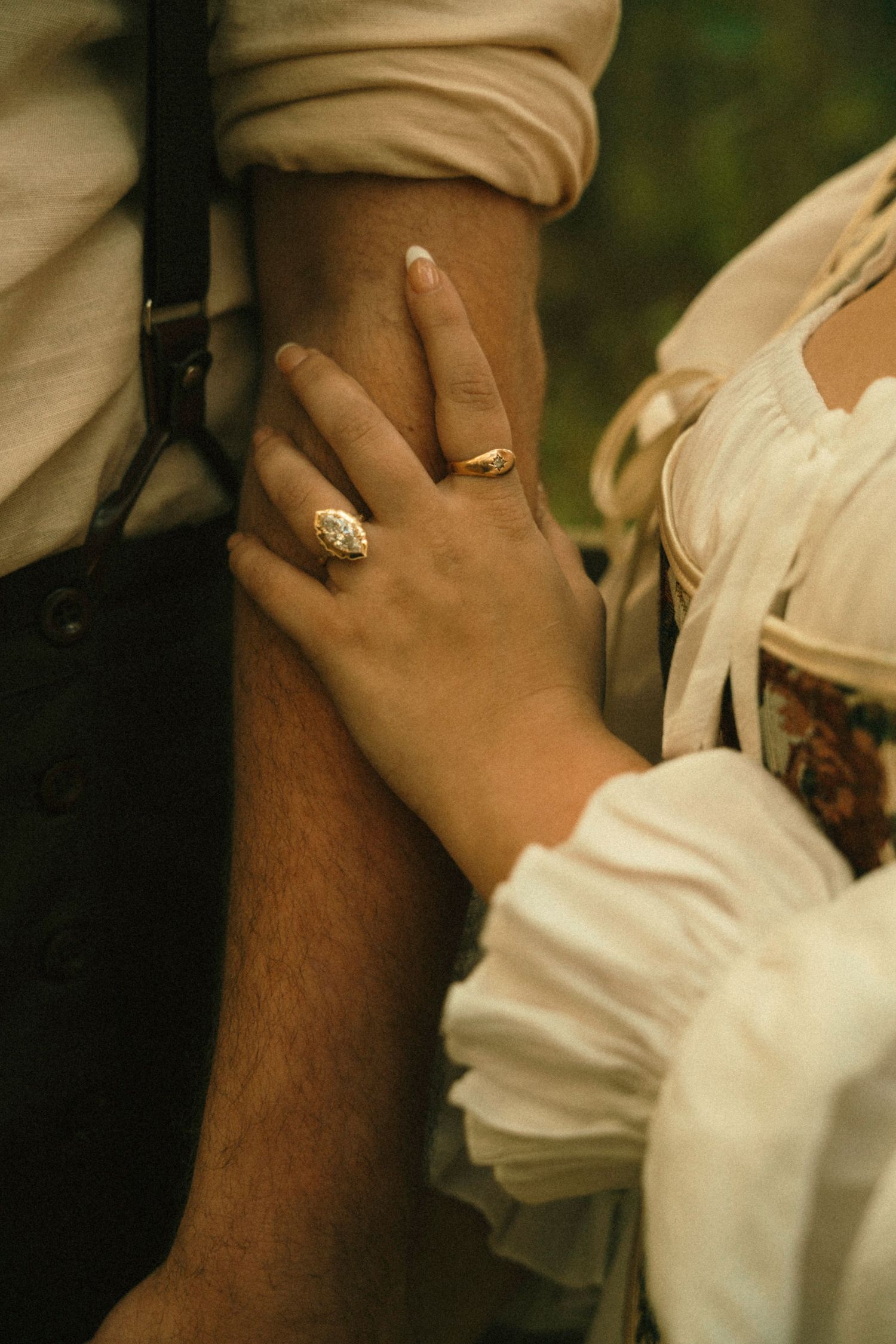 Close-up shot of hands with wedding rings exchanging a tender embrace against a blurred natural background.