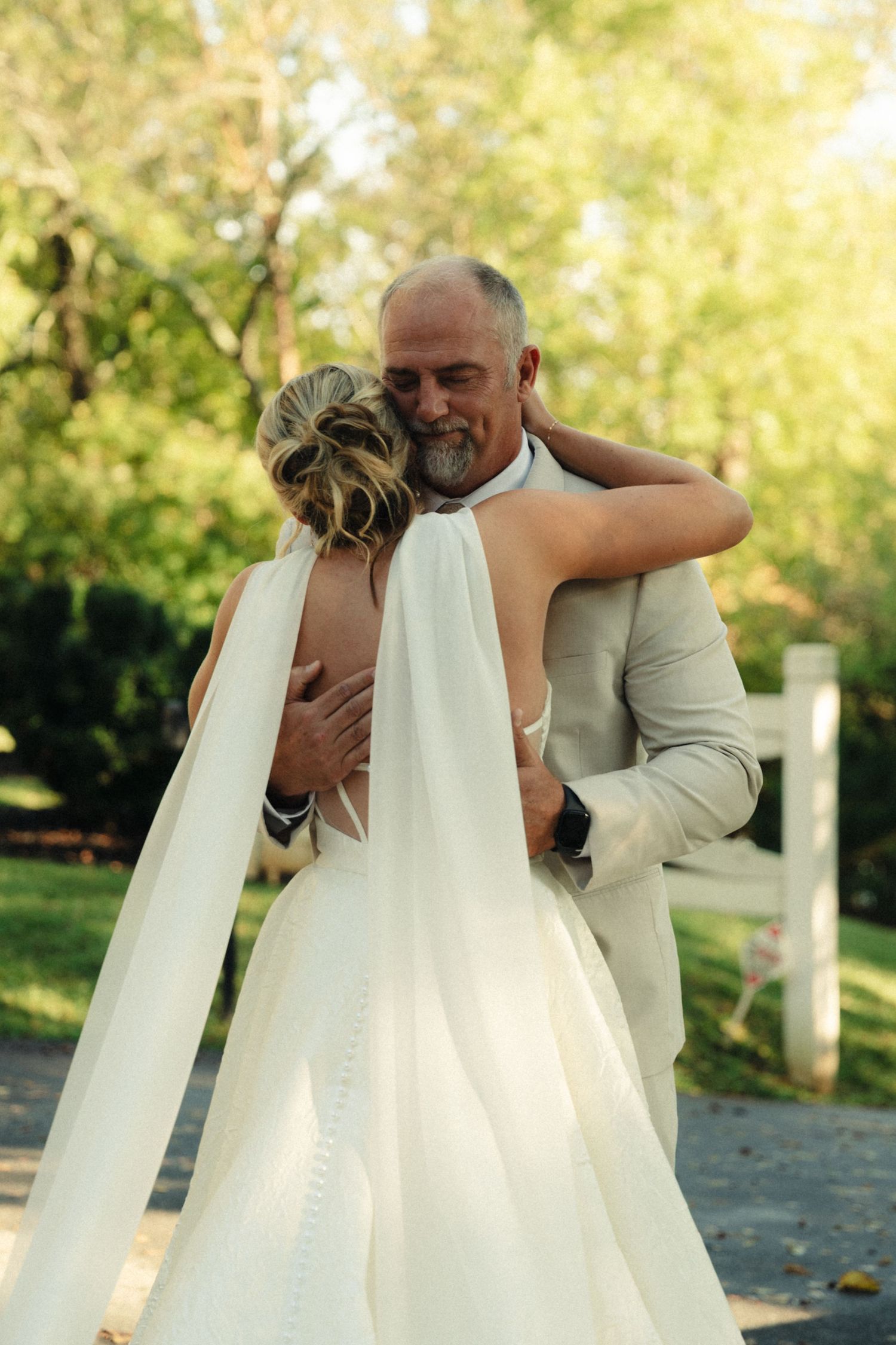 A tender embrace between newlyweds during an outdoor wedding ceremony in a sunlit garden setting.