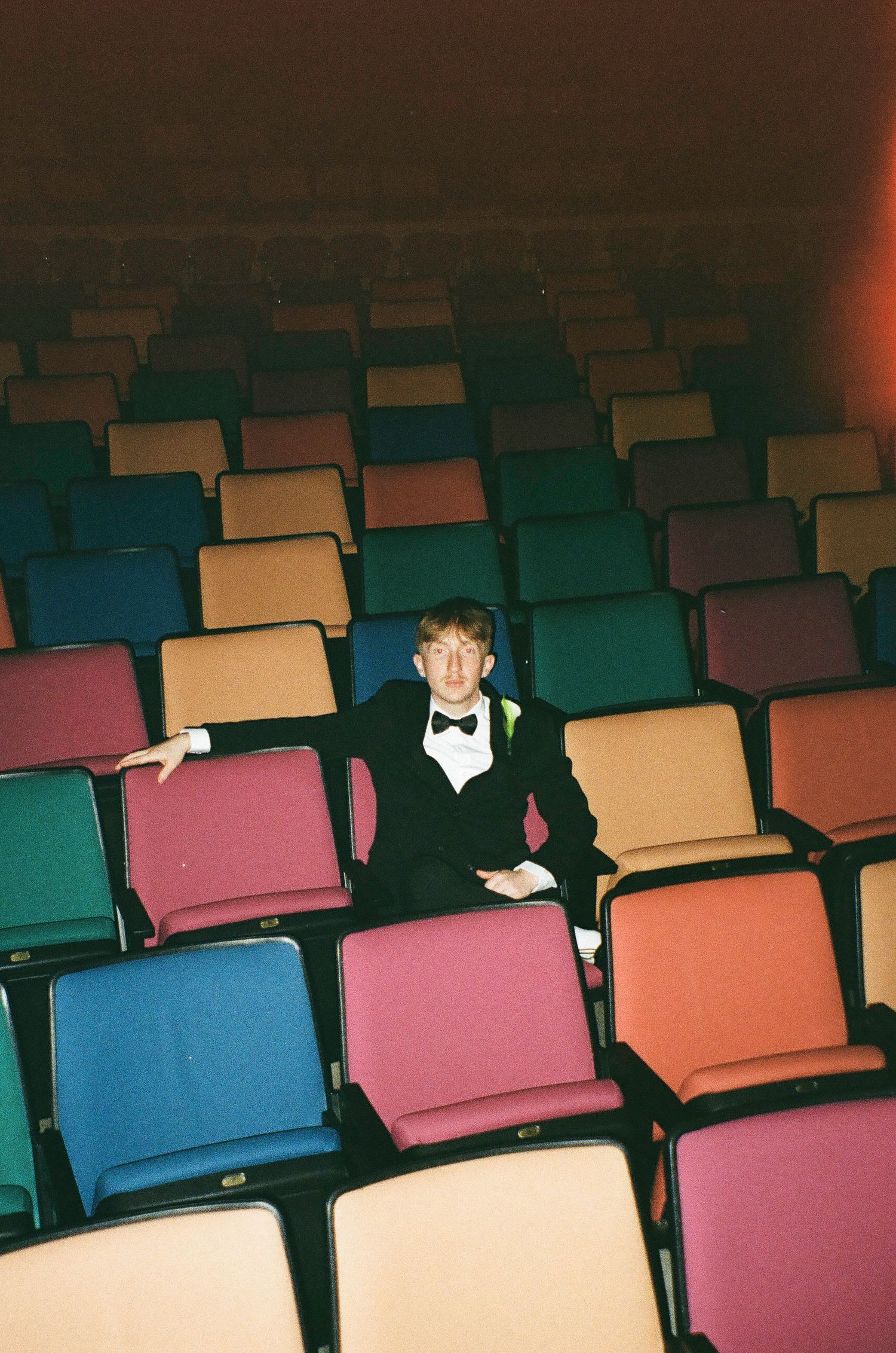 Empty auditorium with colorful seats and a single person sitting in formal attire.