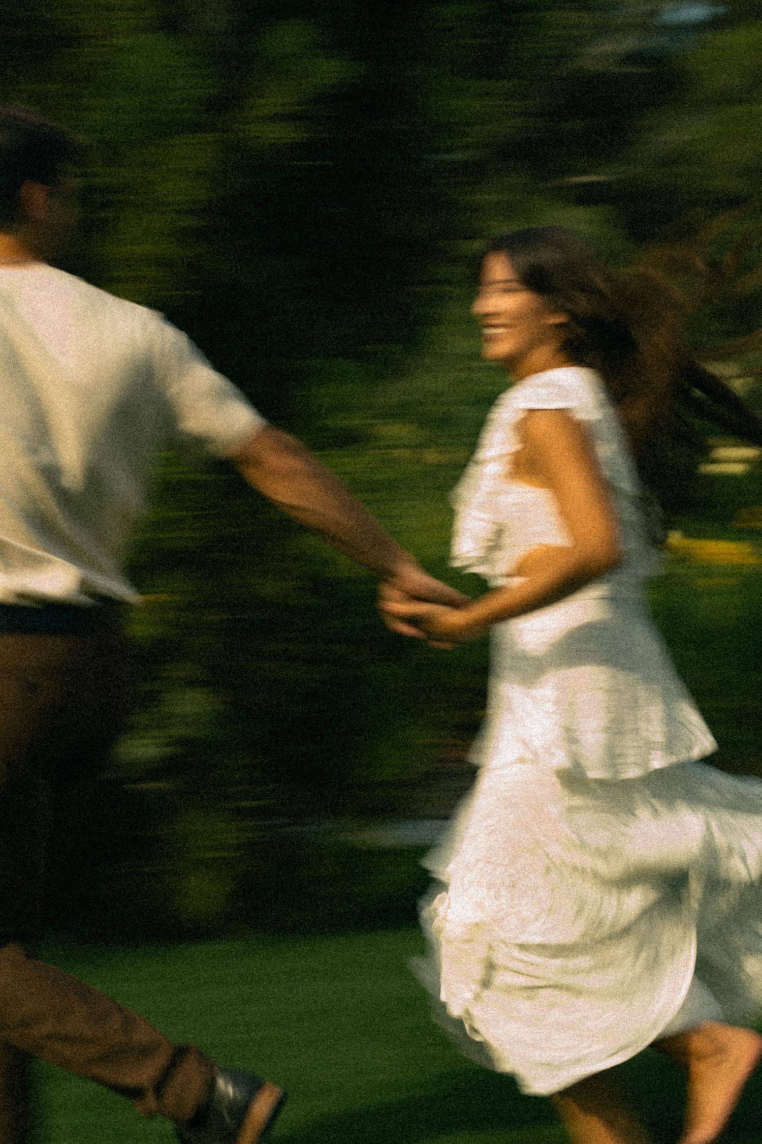 Motion-blurred sequence of people in white clothing running and playing in a garden setting.