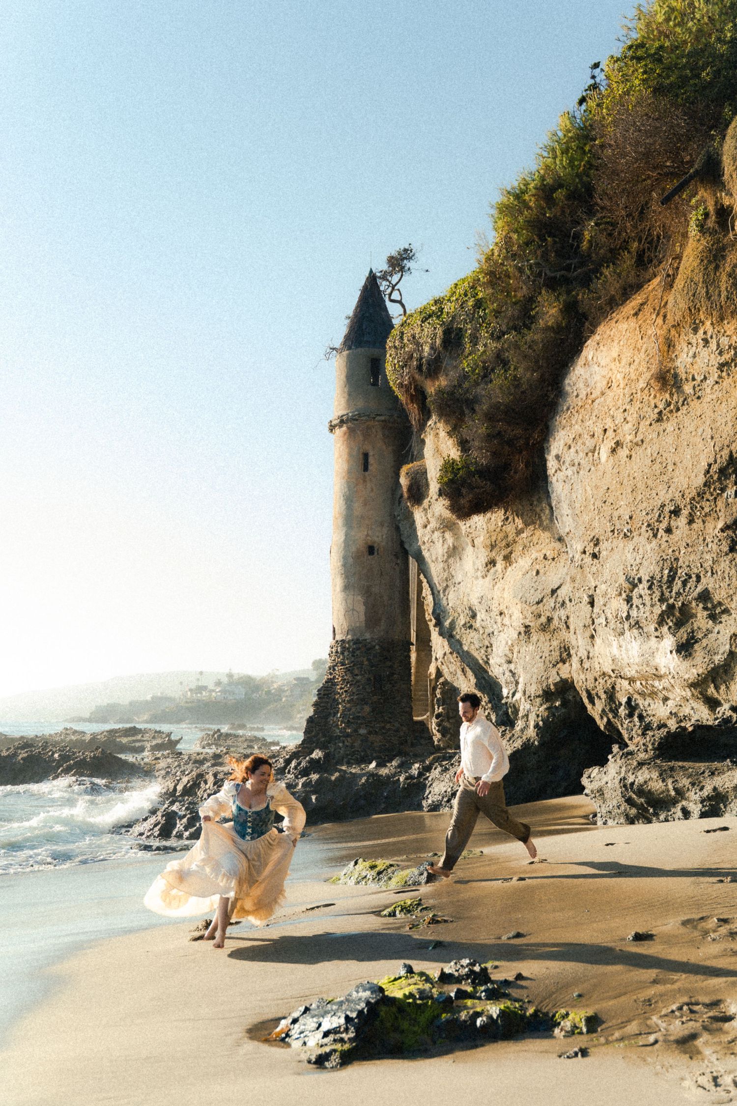 Beach photoshoot sequence near dramatic coastal tower and cliffs.
