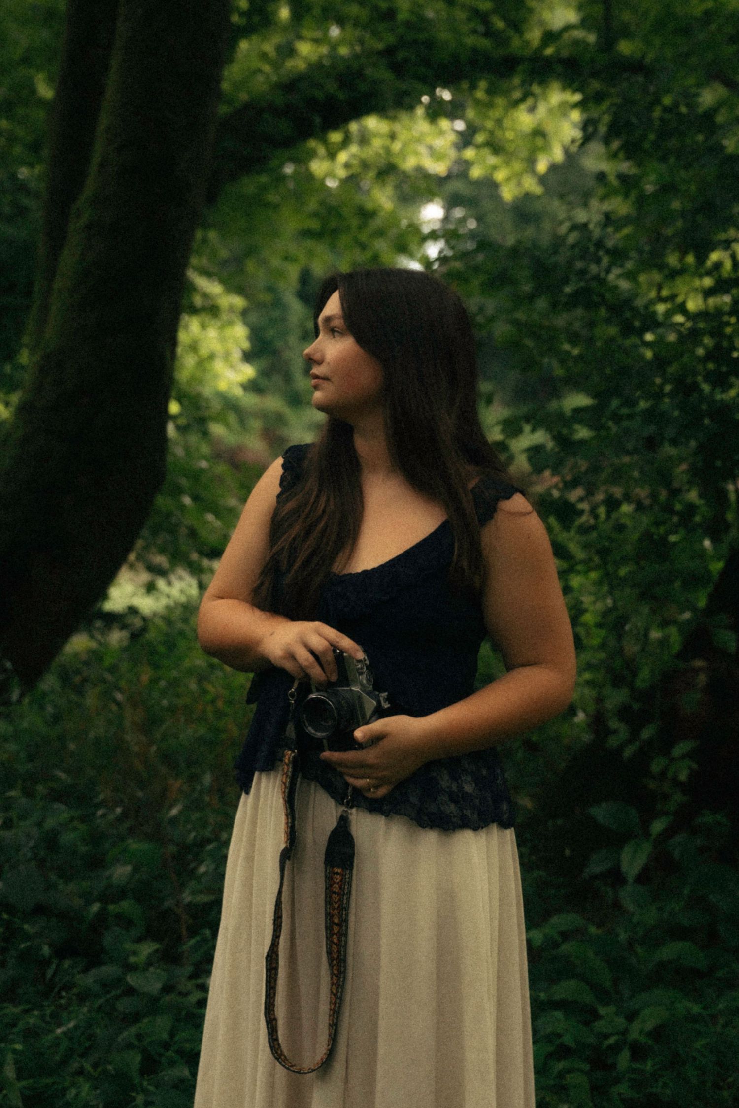 Person in a two-toned dress poses with vintage camera in a forest setting.