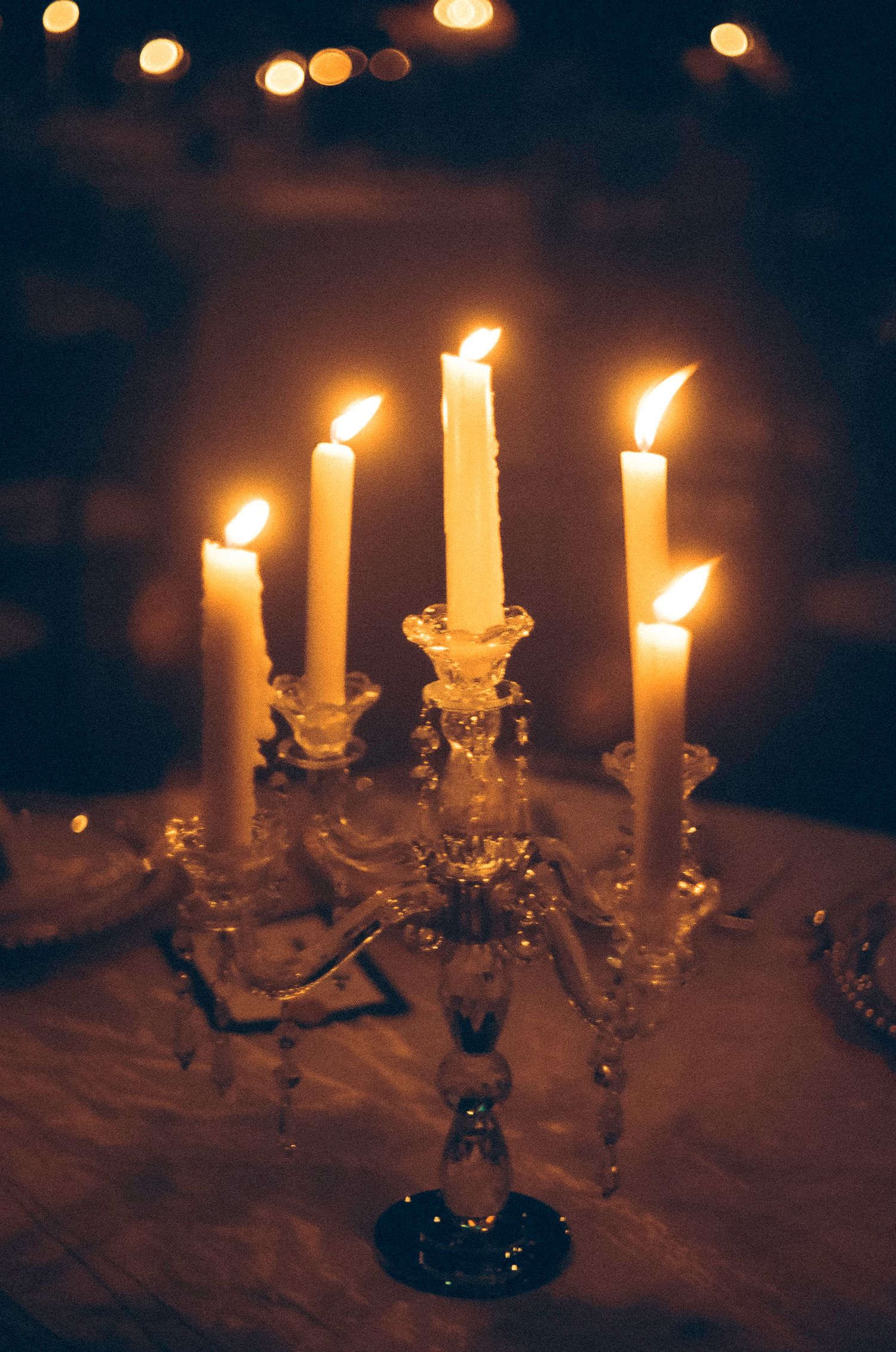 Crystal candelabra with five lit white candles creating a warm, romantic ambiance against a dark background.