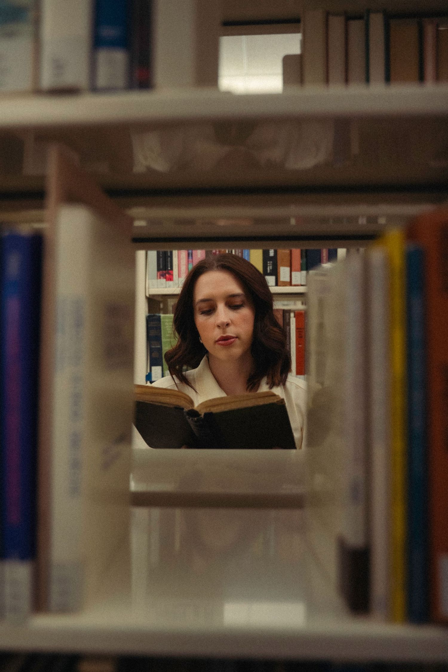 View through library shelves of someone reading between rows of books.