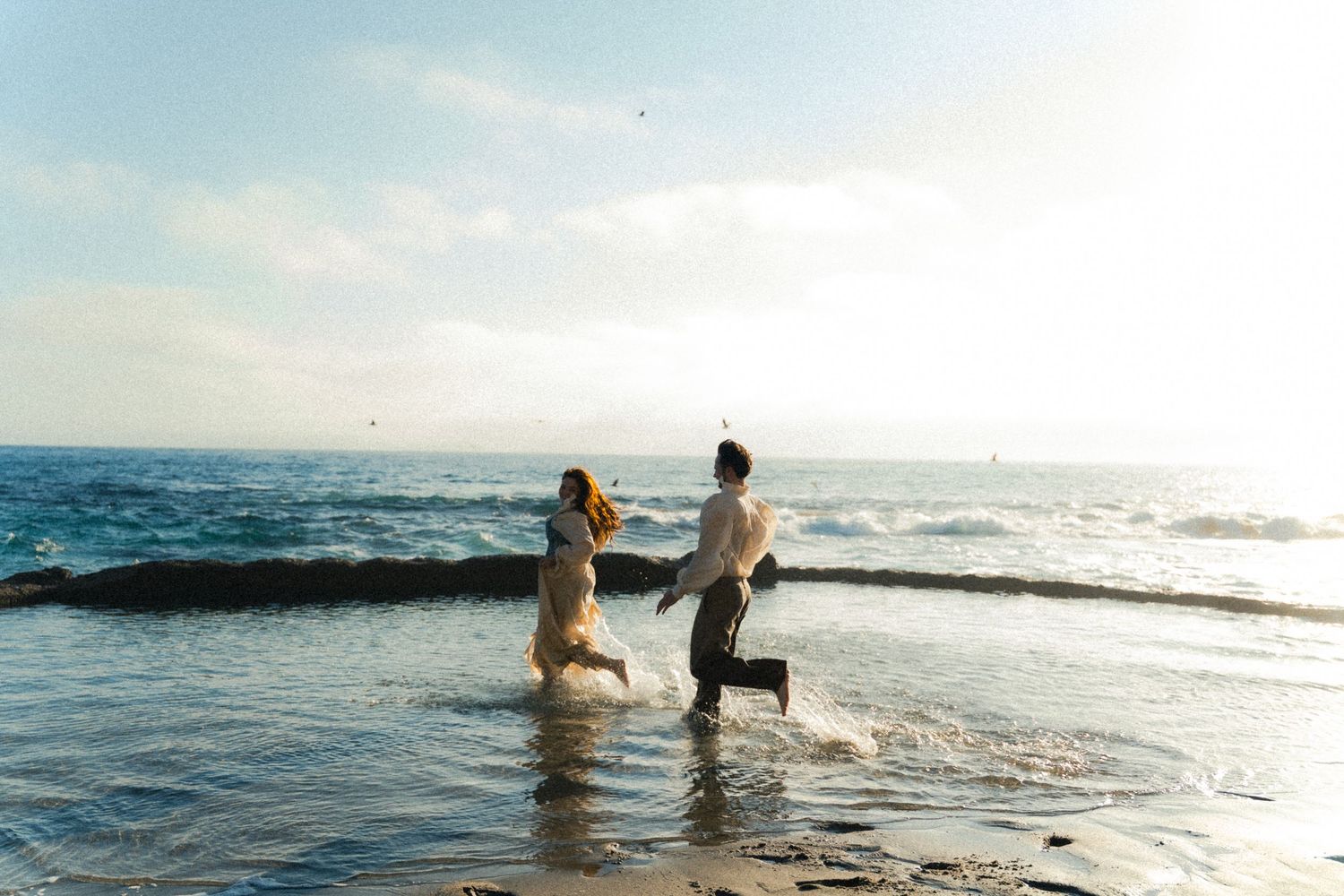 People swimming and playing in the ocean at sunset with waves crashing along a scenic beach shoreline.