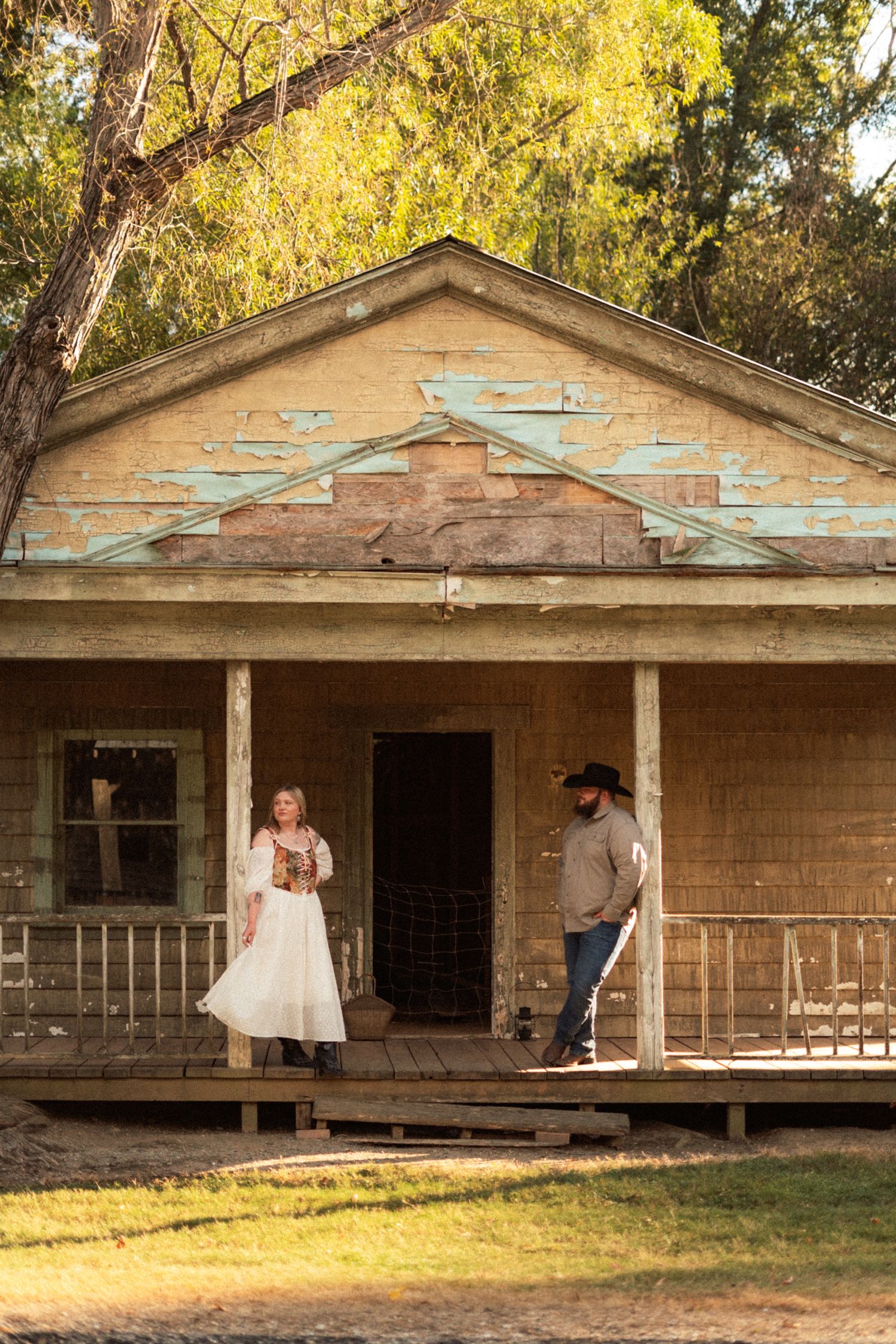 An abandoned rustic building with peeling paint and a weathered porch sits in golden autumn light.