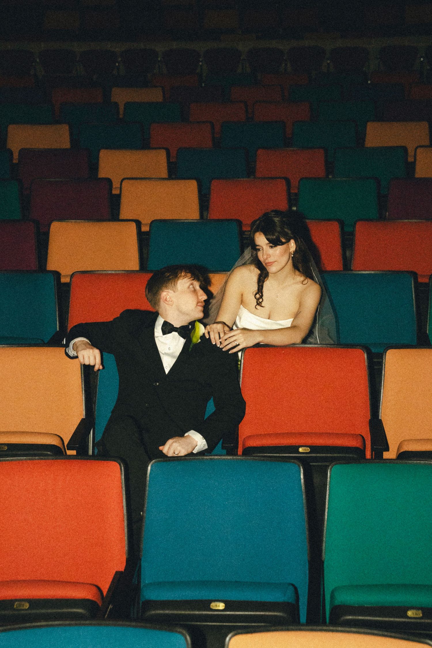 Two people share an intimate conversation in vibrant colored theater seating.
