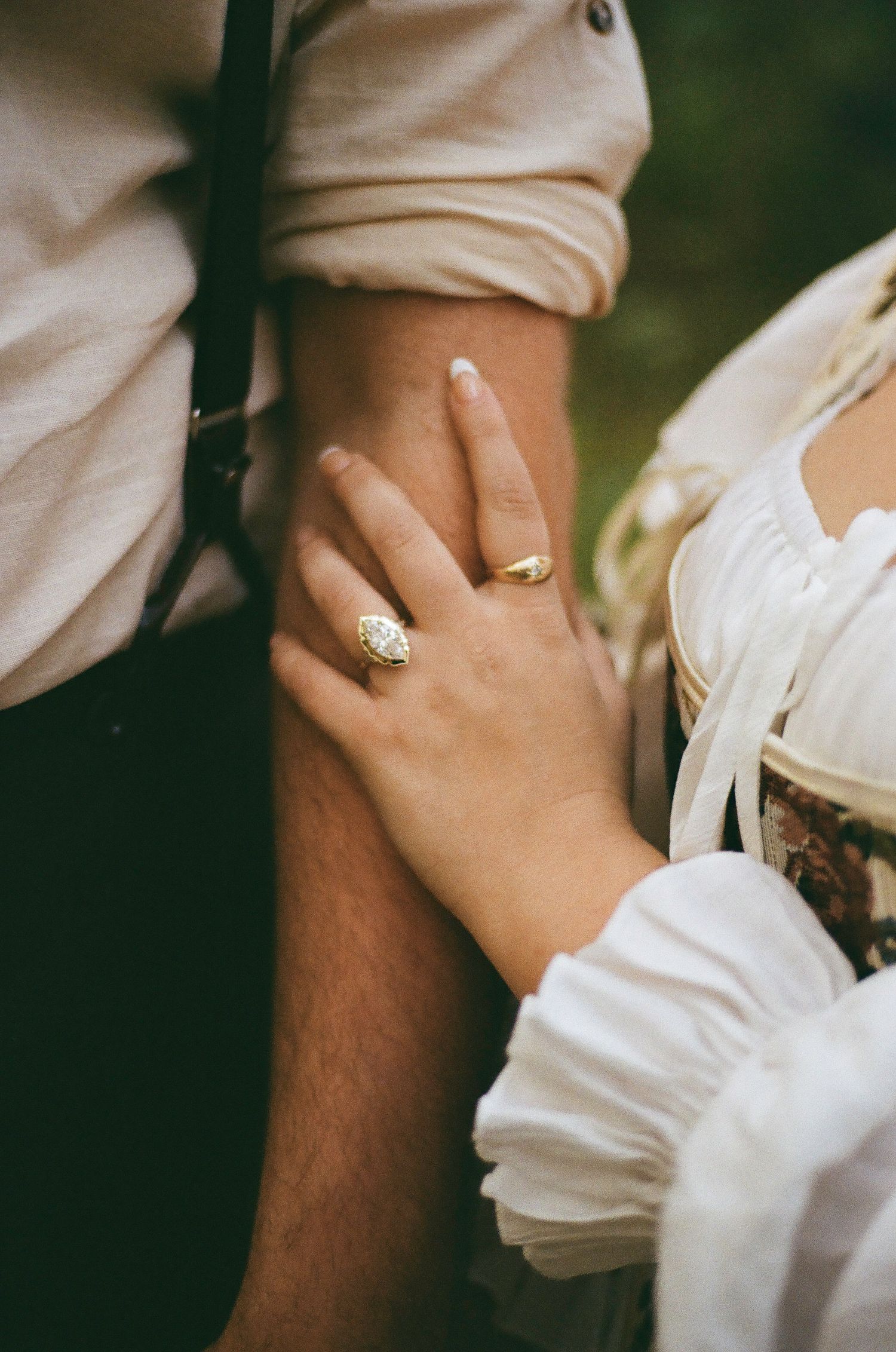 Close-up shot of hands with an engagement ring against white period clothing.