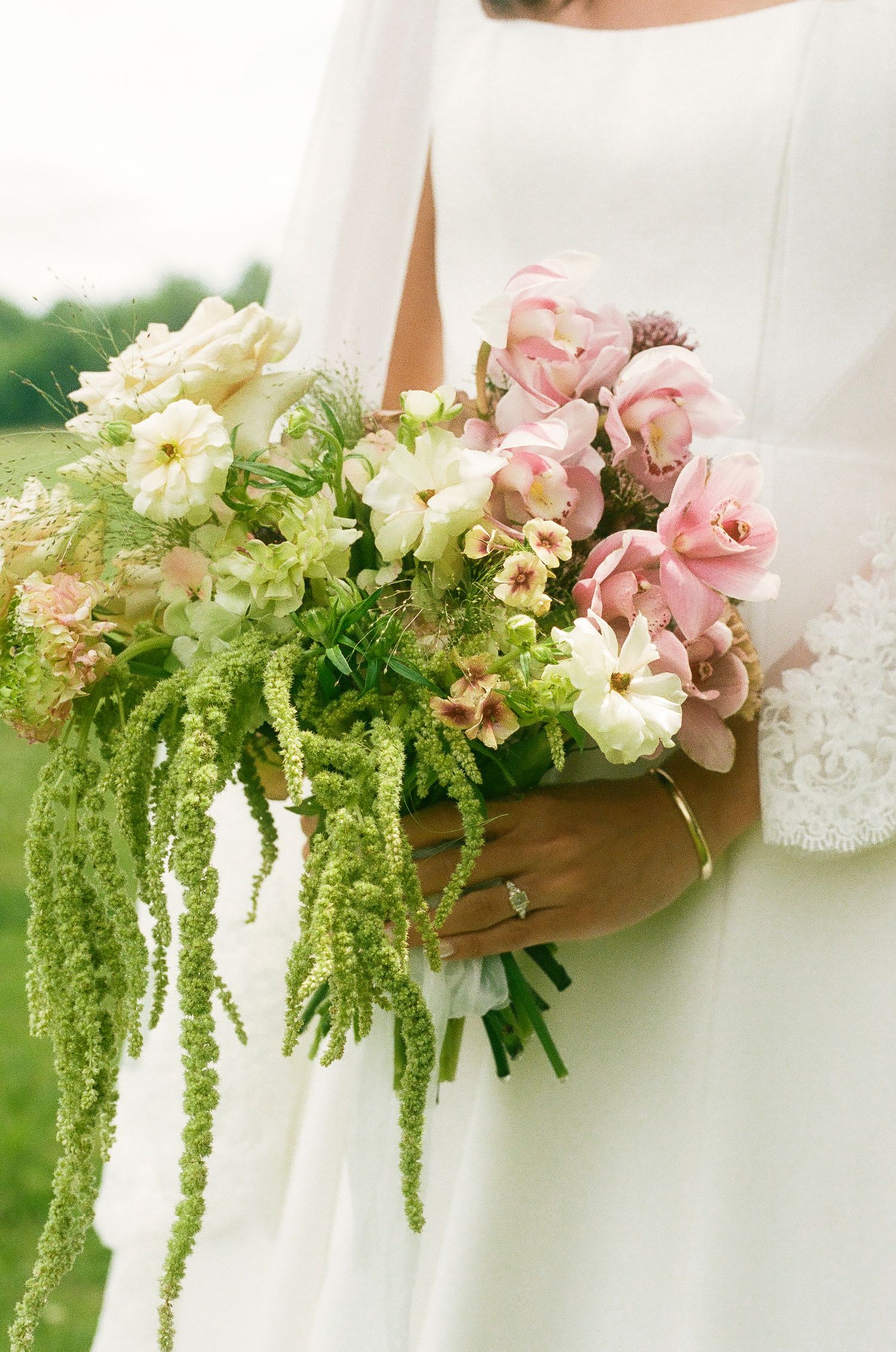 Bride holding lush wedding bouquet with pink tulips, white flowers, and cascading green amaranthus.