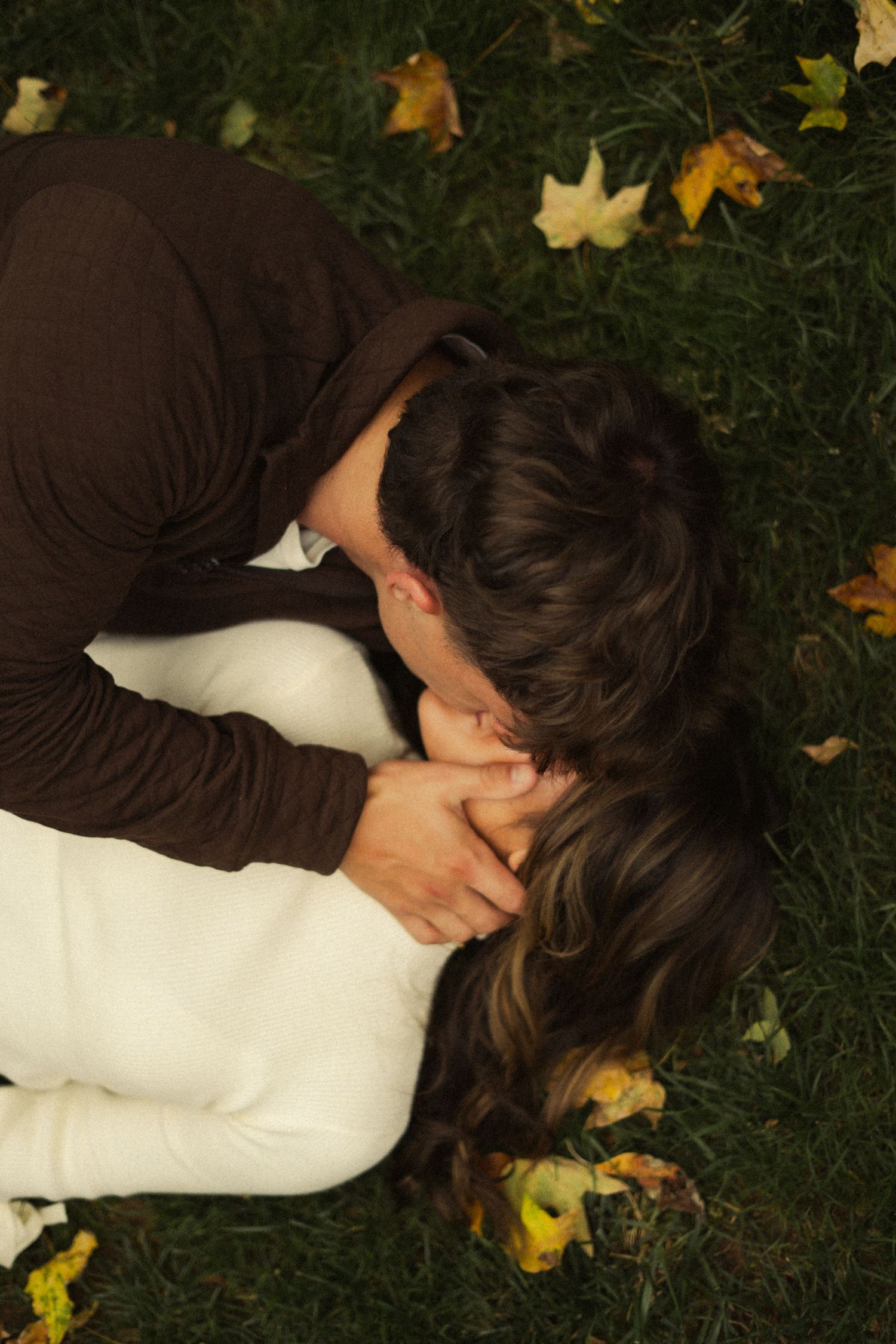 A couple lying on grass covered with autumn leaves.