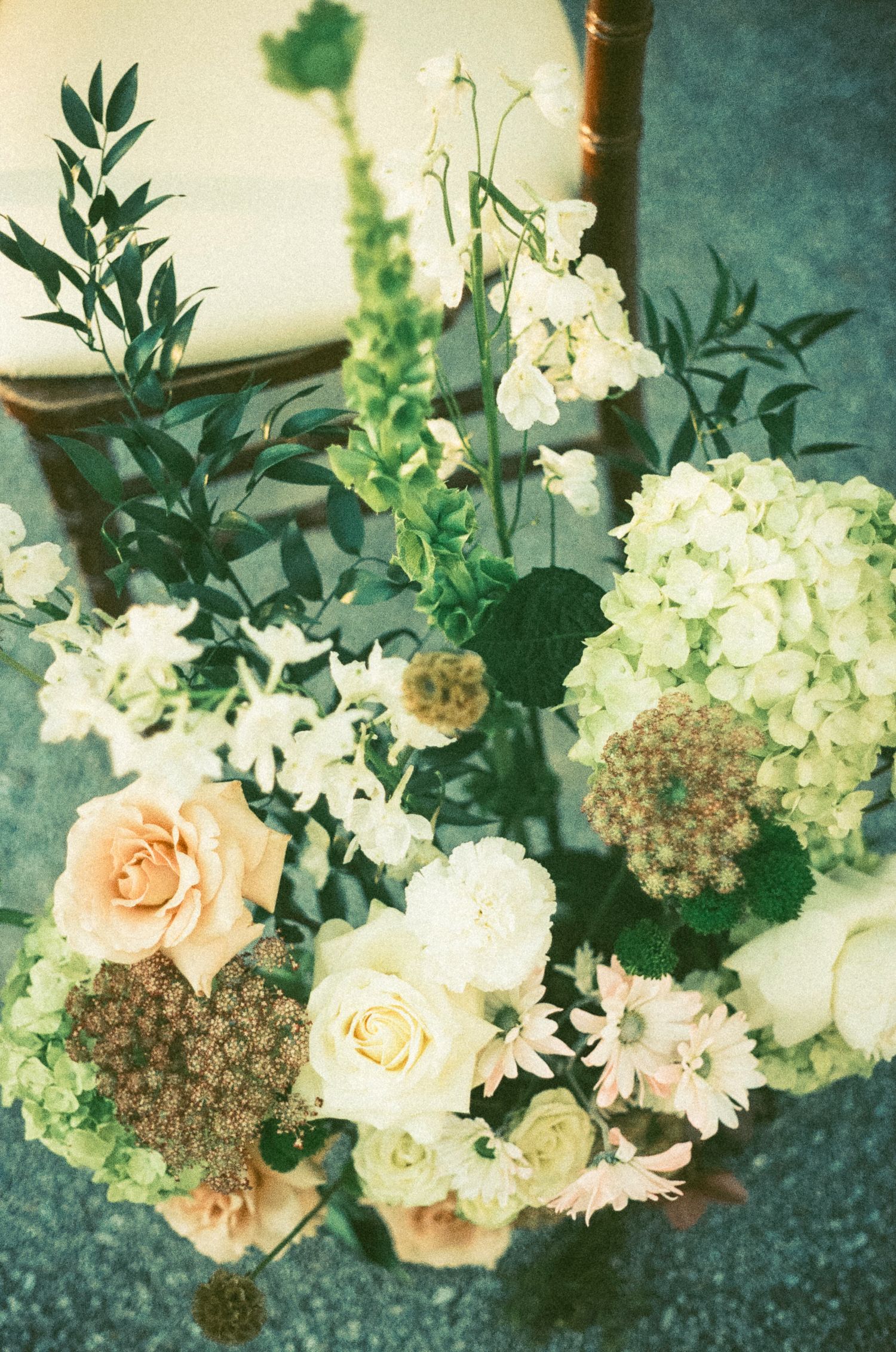 Vintage-style floral arrangement with peach roses, white hydrangeas, and dried seed pods in muted tones.