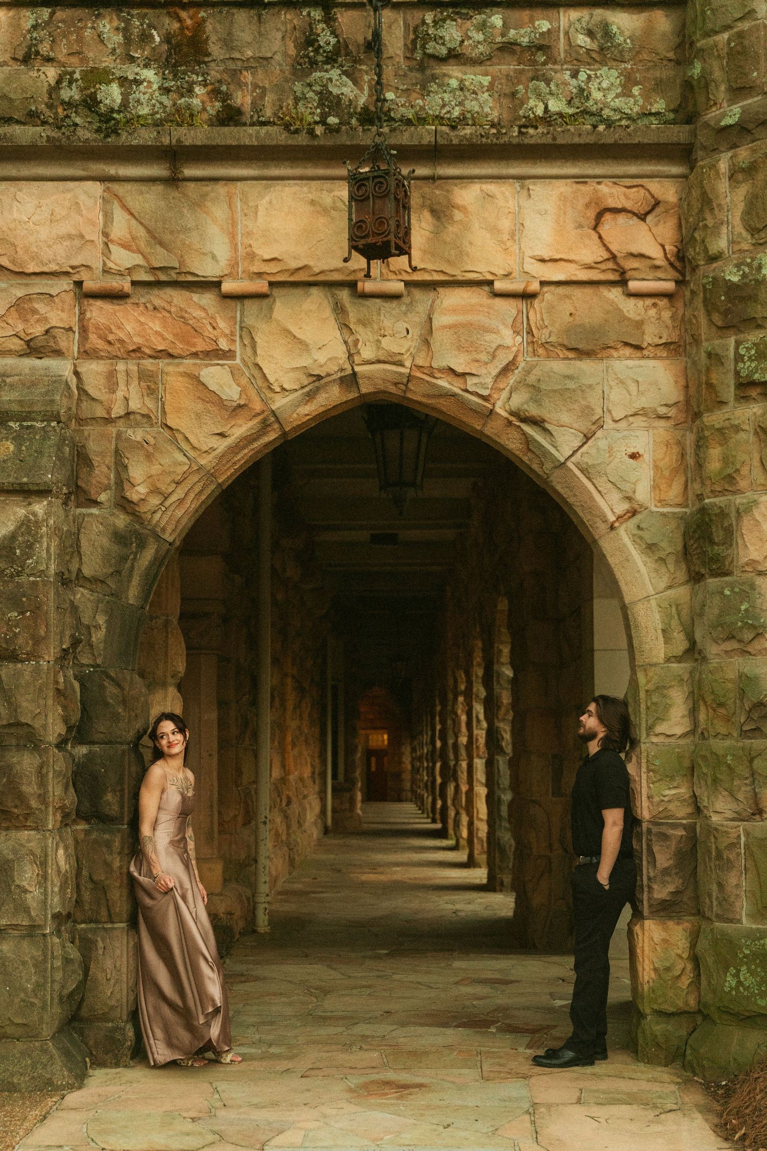 A stone archway corridor with two people standing at opposite ends in dramatic lighting.