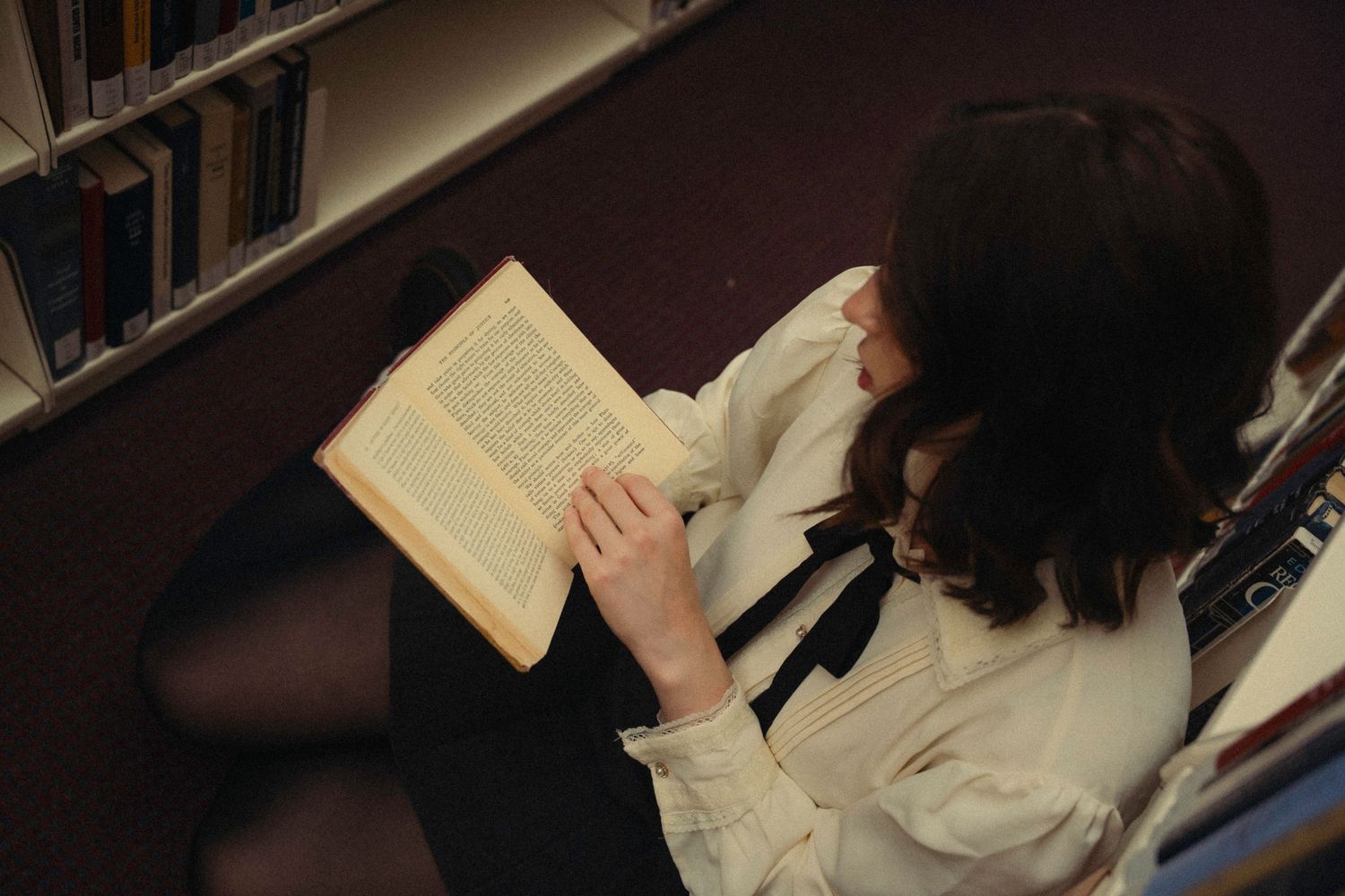Person reading a book while sitting in a dimly lit library or study area.