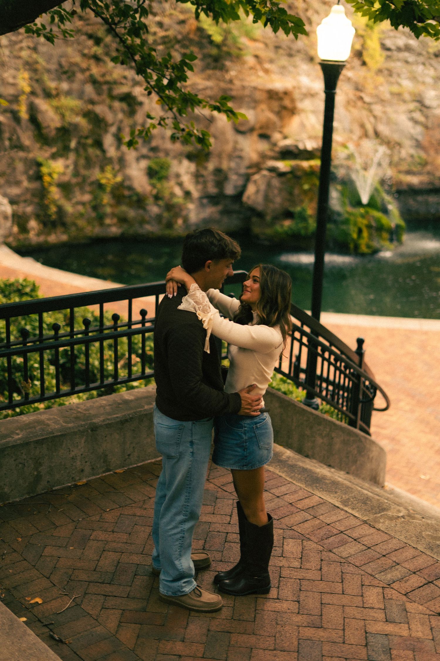 A romantic dance sequence unfolds on a brick terrace overlooking a scenic waterfront at sunset.
