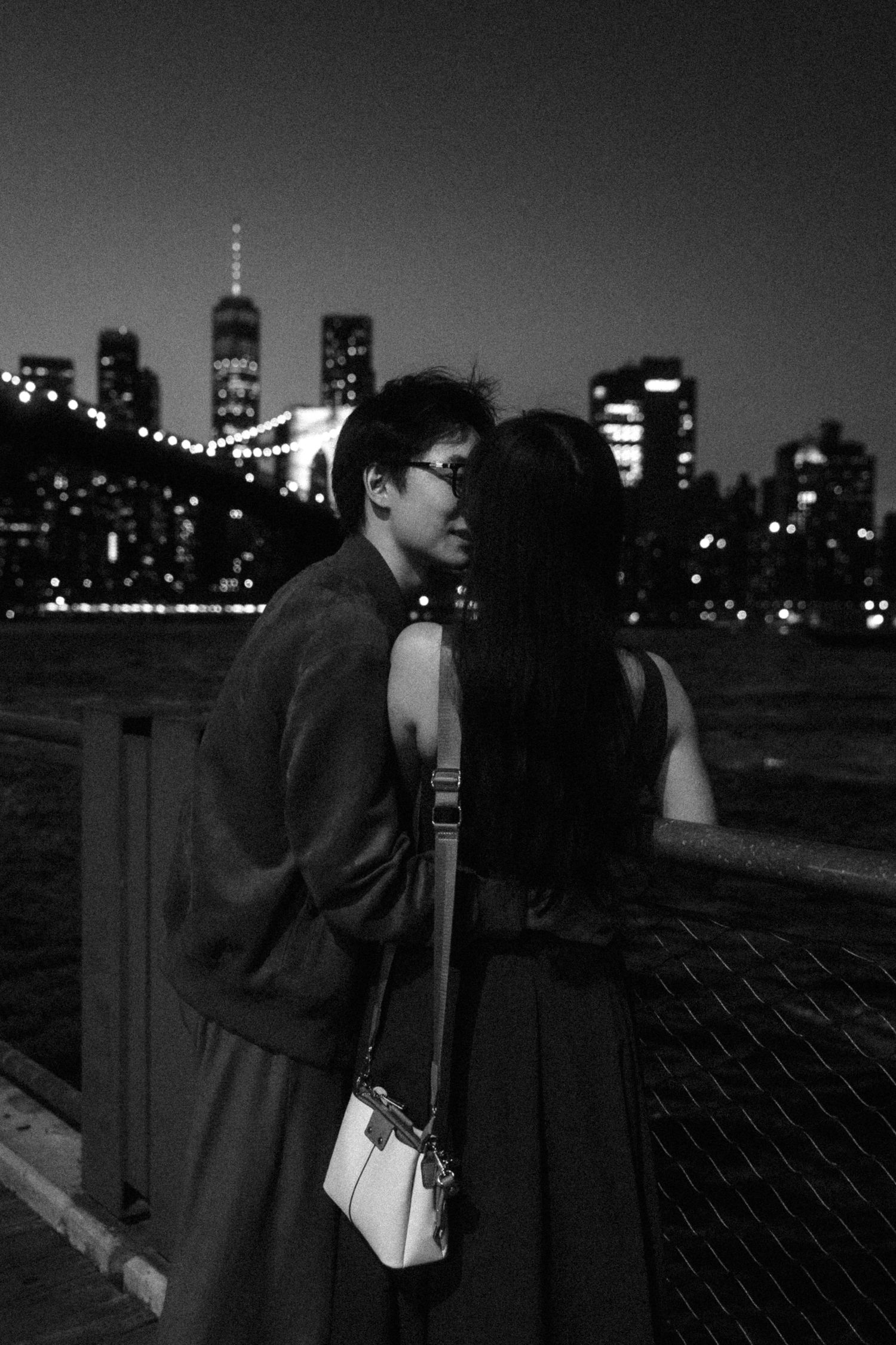 Romantic nighttime silhouette with NYC skyline and Brooklyn Bridge lights in background.