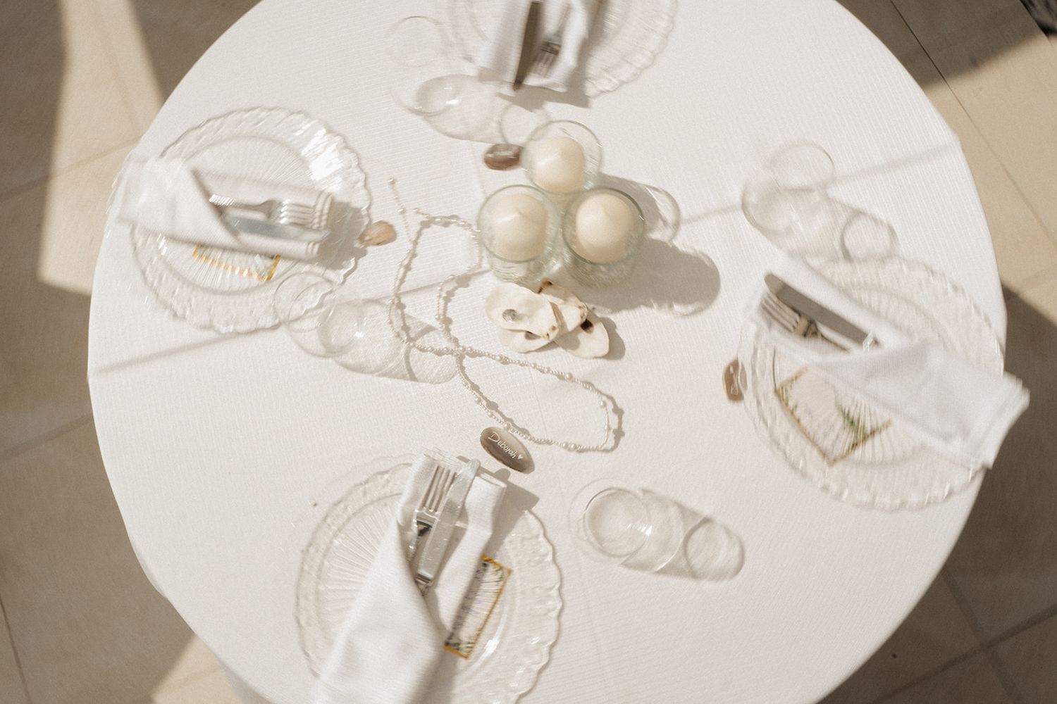 Elegant white round table set with glass plates, napkins, and decorative spheres in a minimalist tablescape.