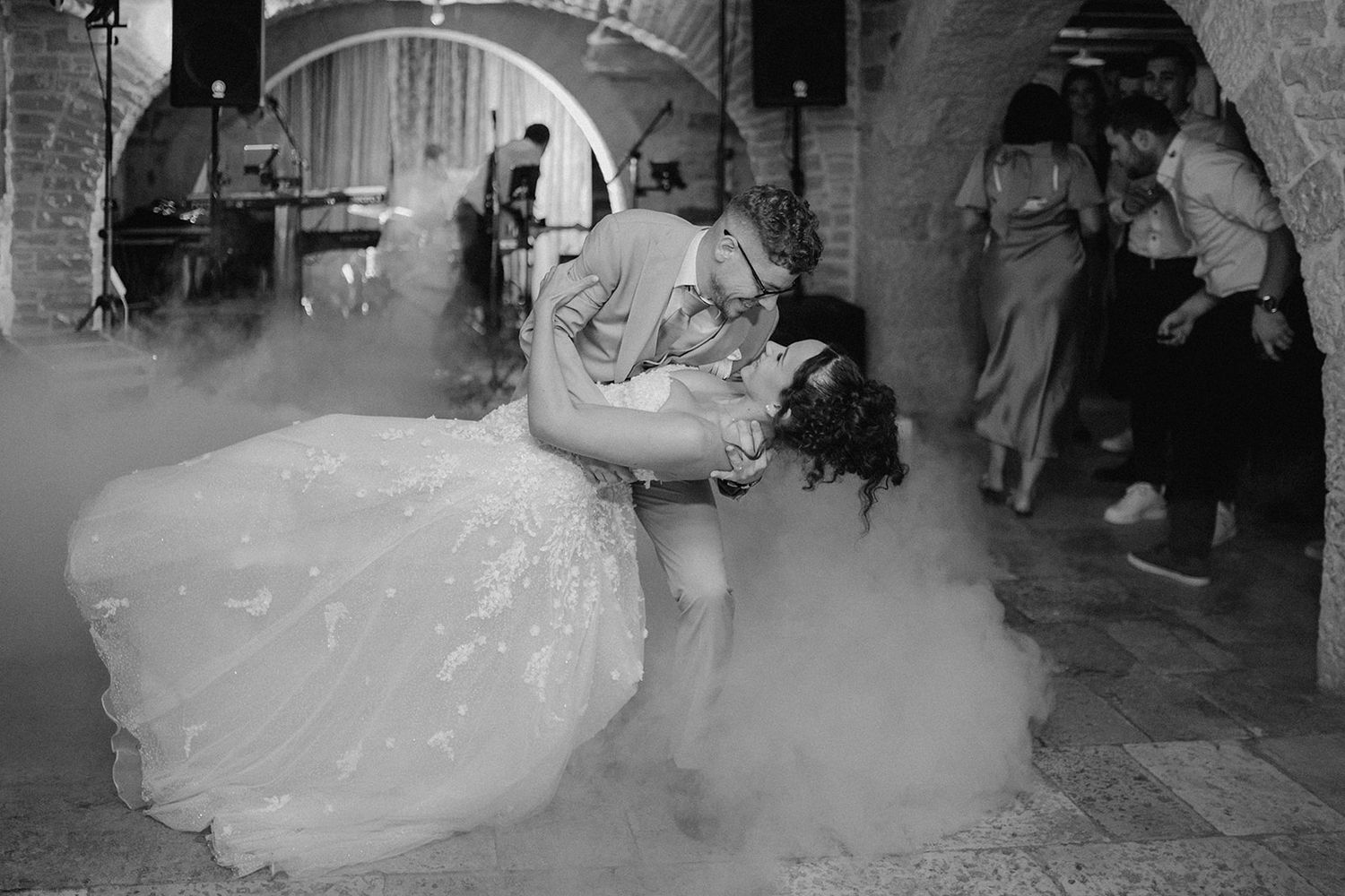 Black and white photo of bride and groom sharing a romantic dip dance surrounded by dramatic fog at their wedding reception.