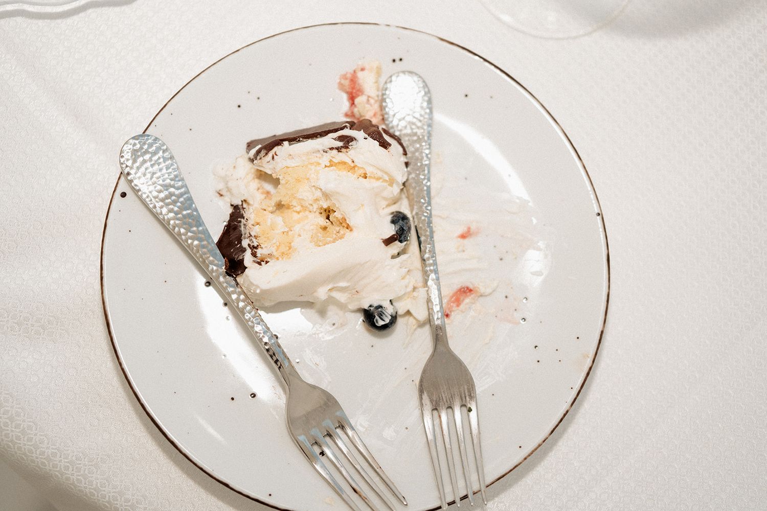 Partially eaten wedding cake slice on white plate with silver forks after reception.