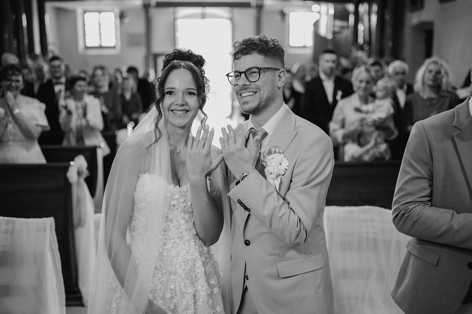 Black and white photo of a joyful bride and groom clapping at the altar during their church wedding ceremony.