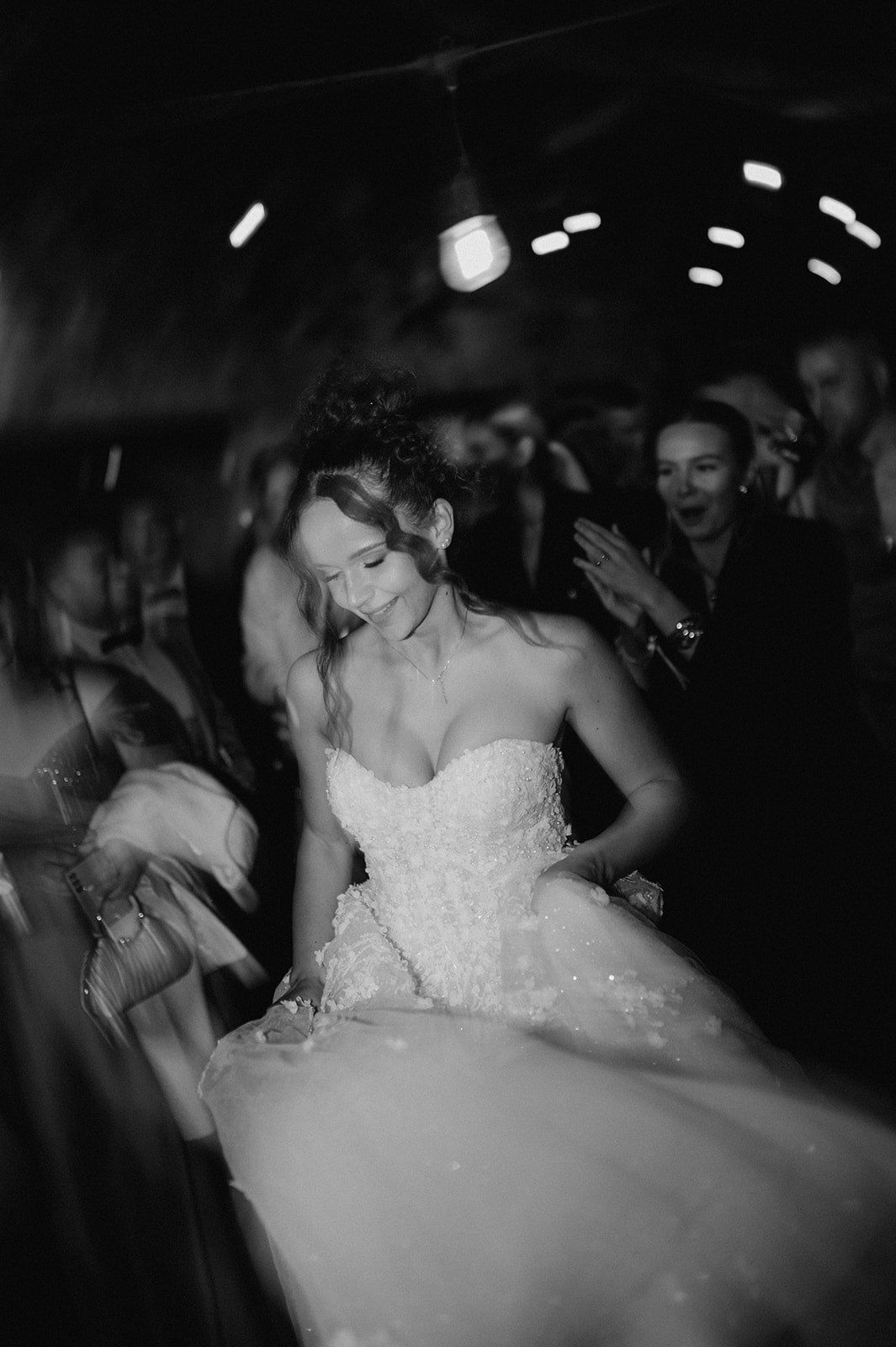 Black and white photo of a bride in a strapless ballgown dancing joyfully at her wedding reception.