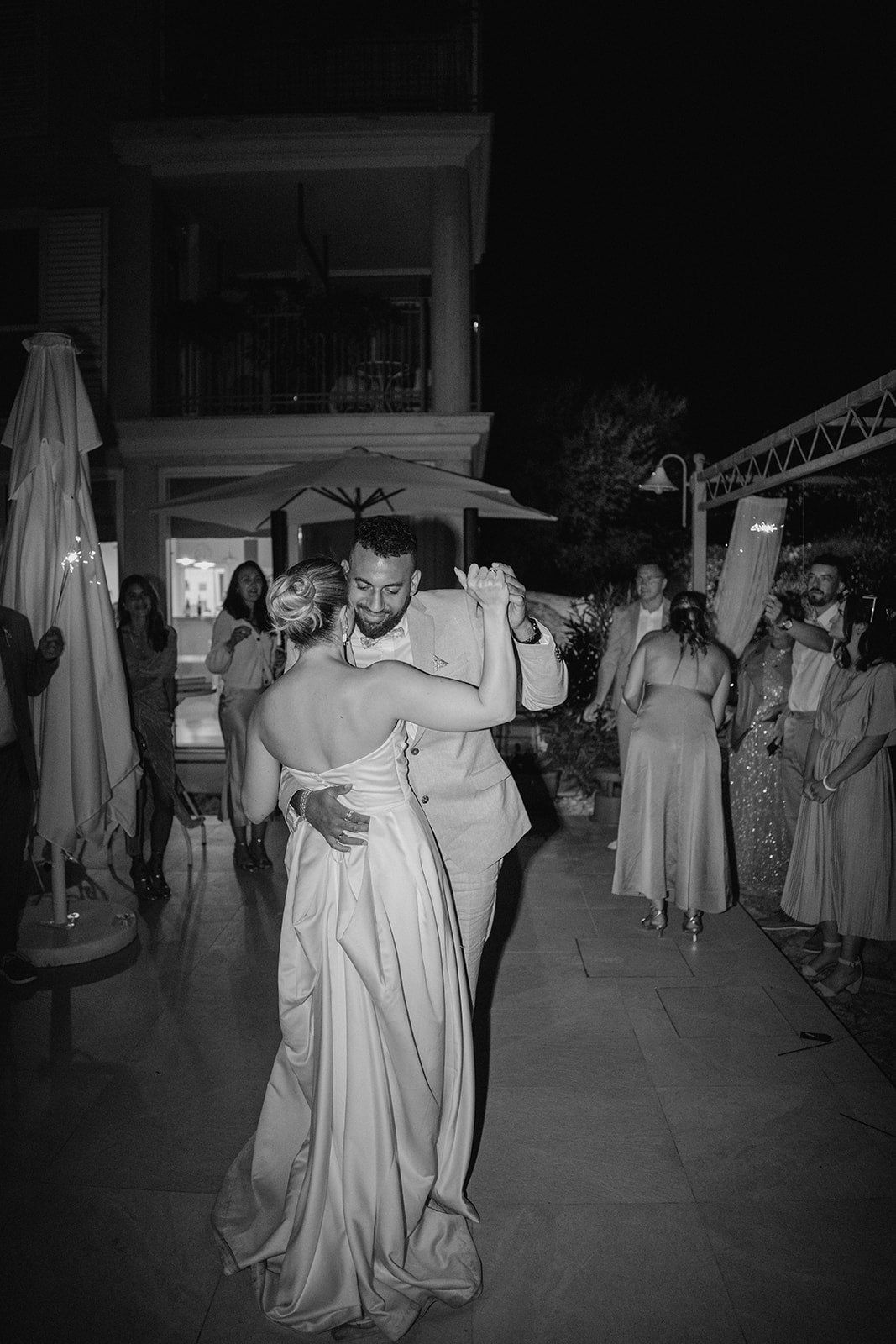 Bride and groom share an intimate first dance embrace at an outdoor evening wedding reception in black and white photo.
