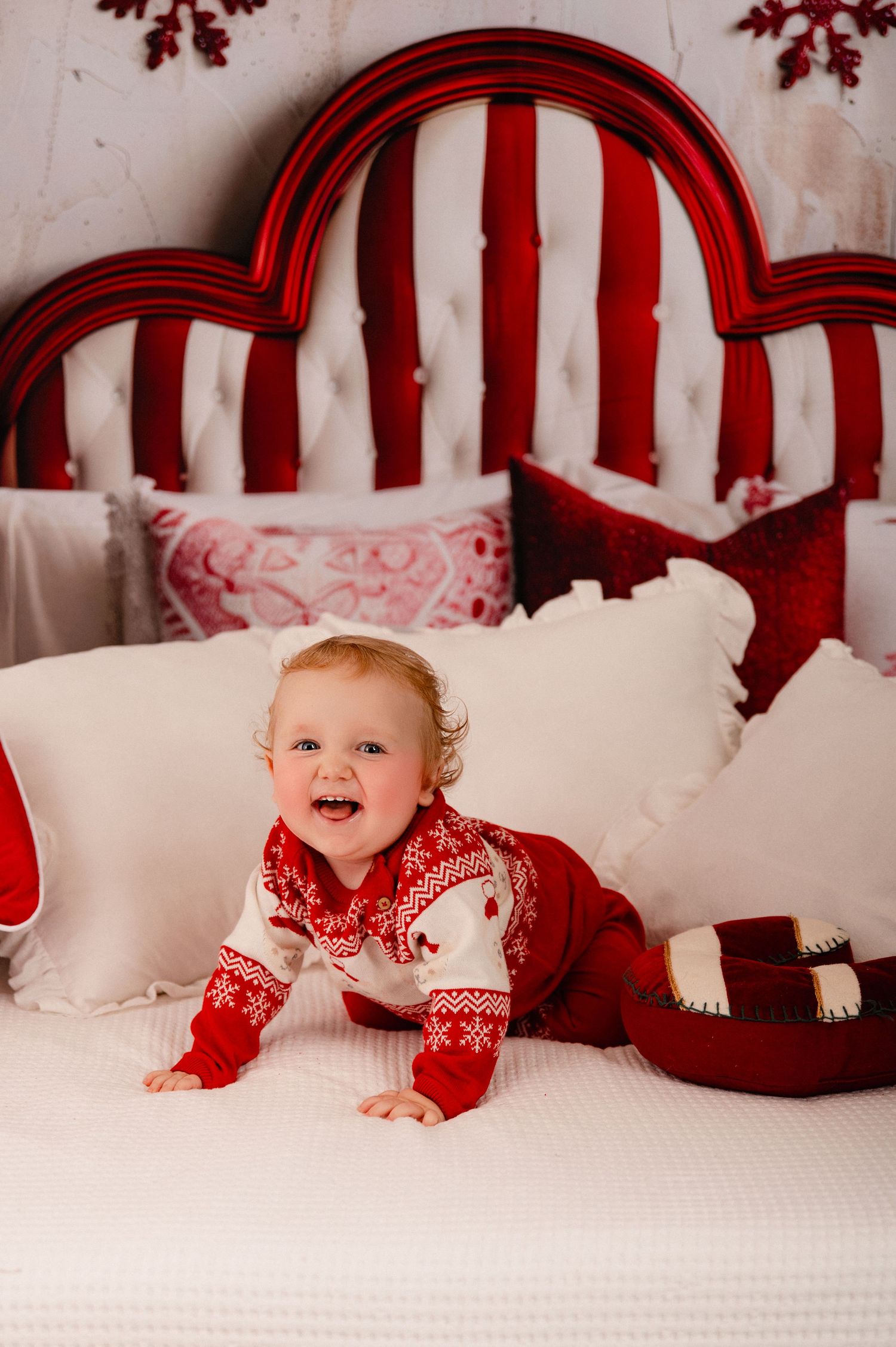 A festive holiday scene with red and white striped headboard, white bedding, and decorative Christmas pillows.