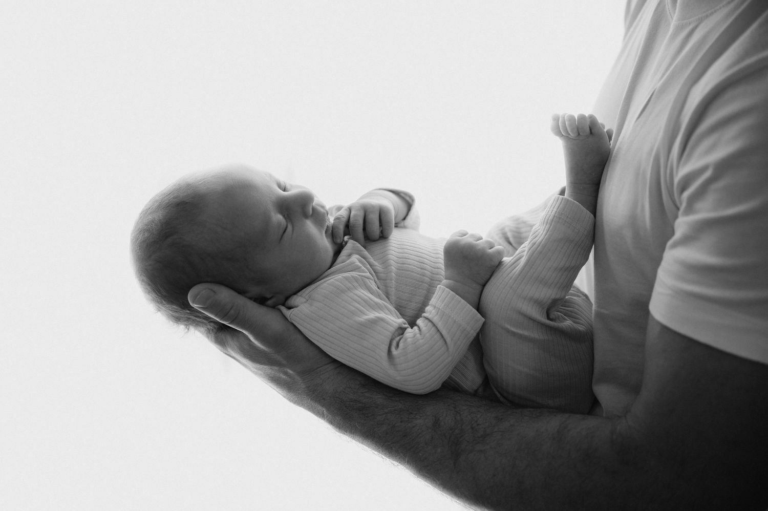 Black and white photo of a baby resting on someone's arm while sucking their thumb.