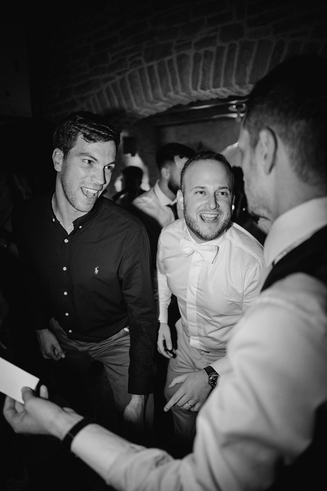 Black and white photo of three men laughing and socializing at a wedding reception party.