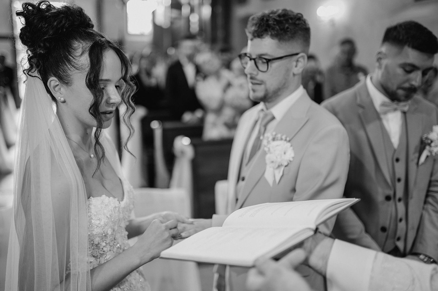 Black and white wedding ceremony photo of bride and groom exchanging vows in a church.