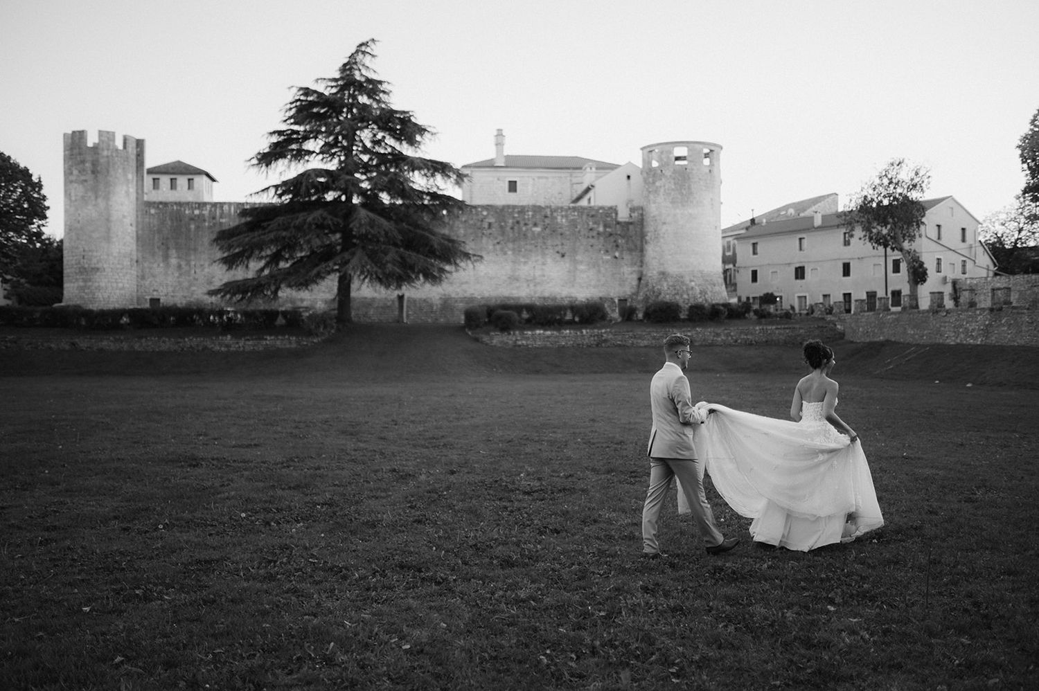 Black and white photo of couple with wedding dress near historic castle at dusk.