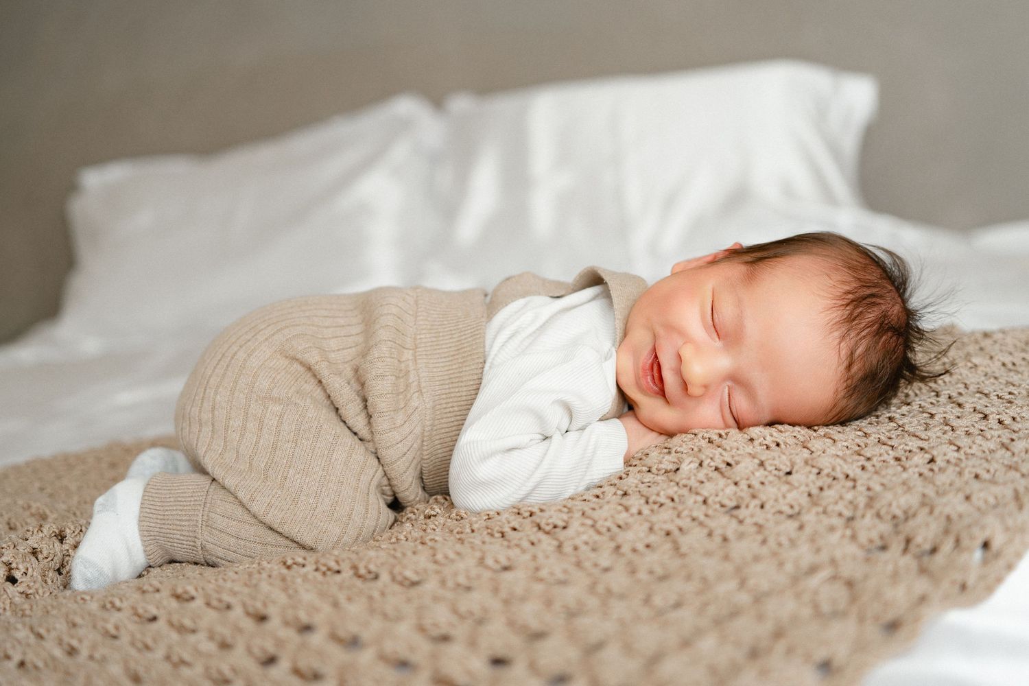 Sleeping newborn wrapped in cozy beige blanket on textured knit surface.