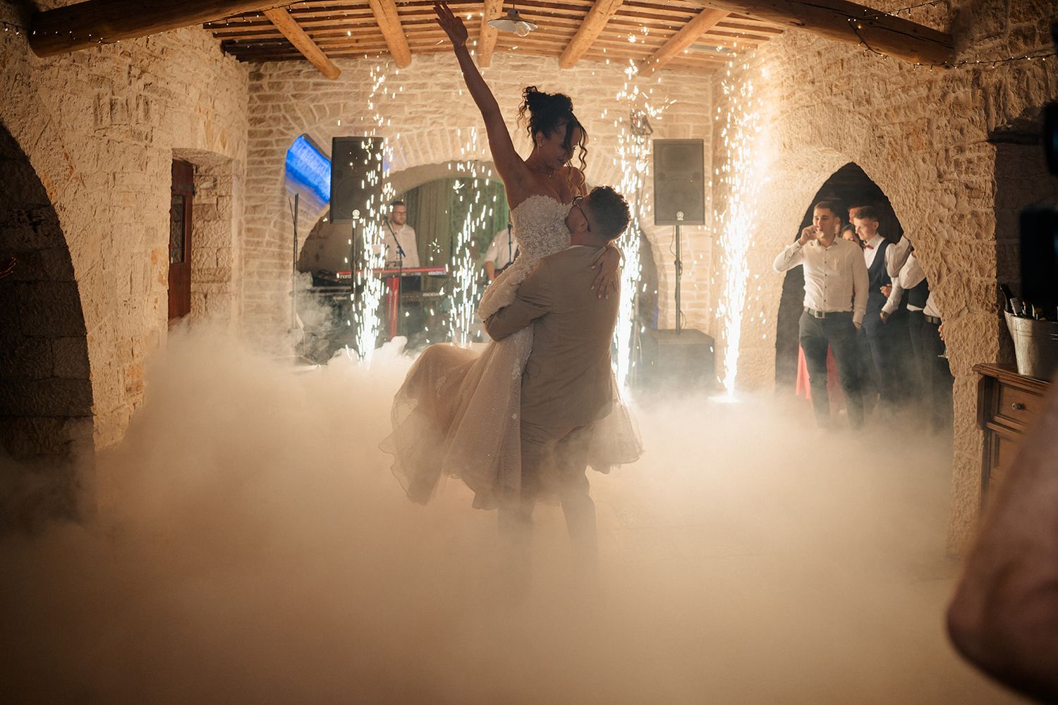 Couple shares first dance surrounded by dramatic fog and sparkling fireworks in a rustic stone wedding venue.
