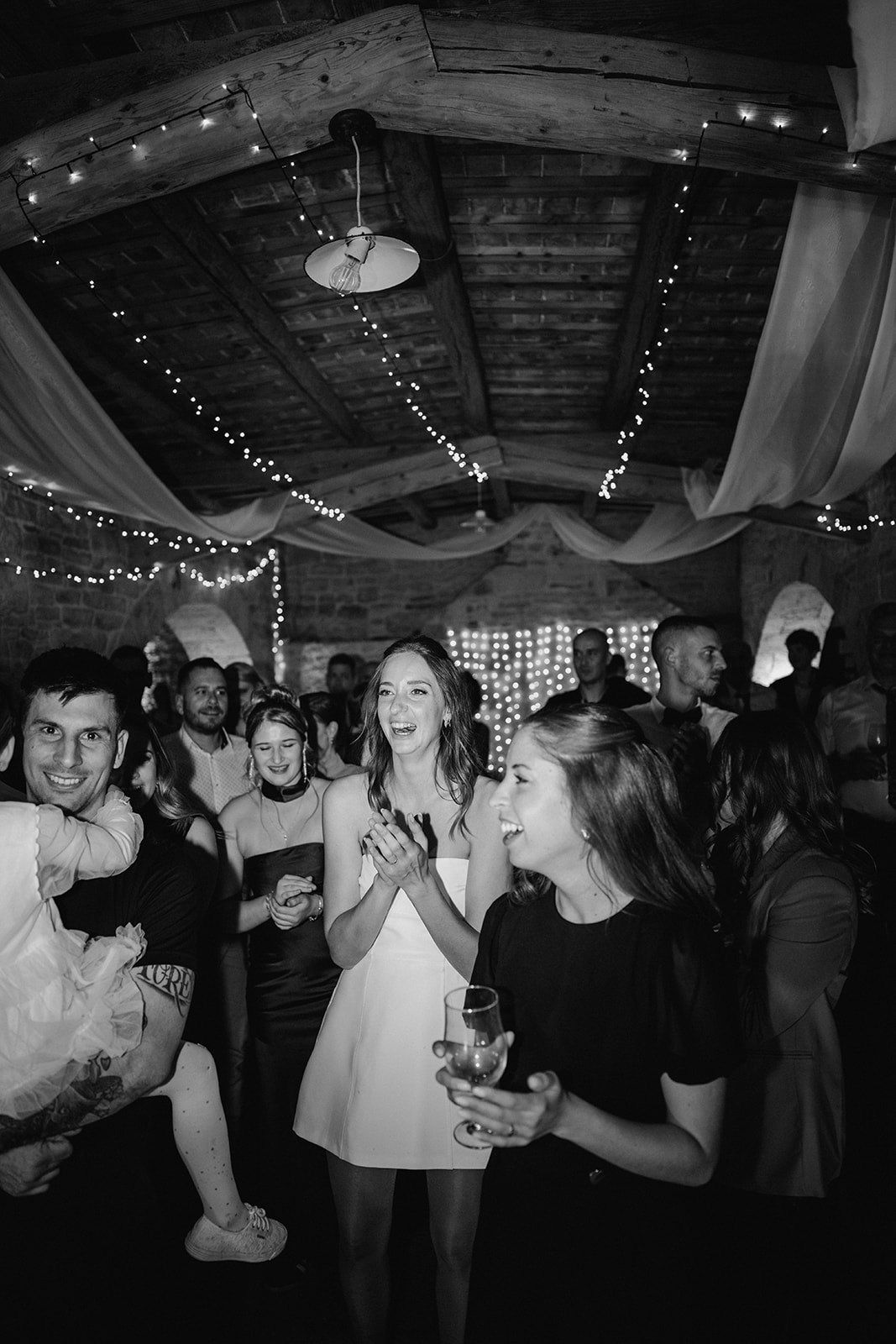 Guests dancing and celebrating joyfully at a wedding reception in a rustic barn with fairy lights.