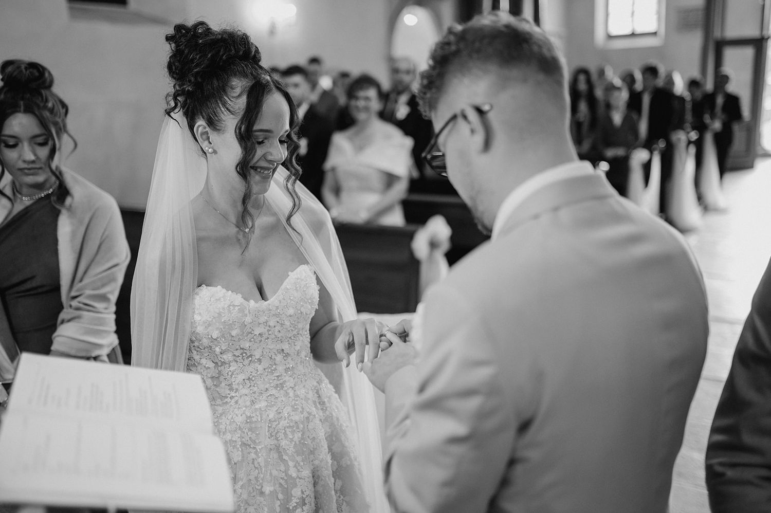 Black and white wedding ceremony photo of bride and groom exchanging rings at the altar in a church.