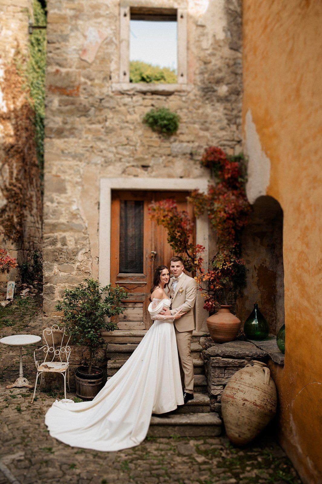 A bride and groom pose on rustic stone steps beside large terracotta urns at a charming Italian villa wedding.