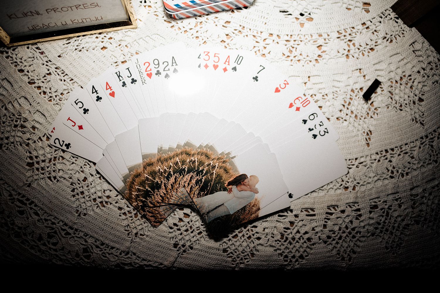 A fan of playing cards spread on a lace tablecloth with scattered cards and game pieces in dim lighting.