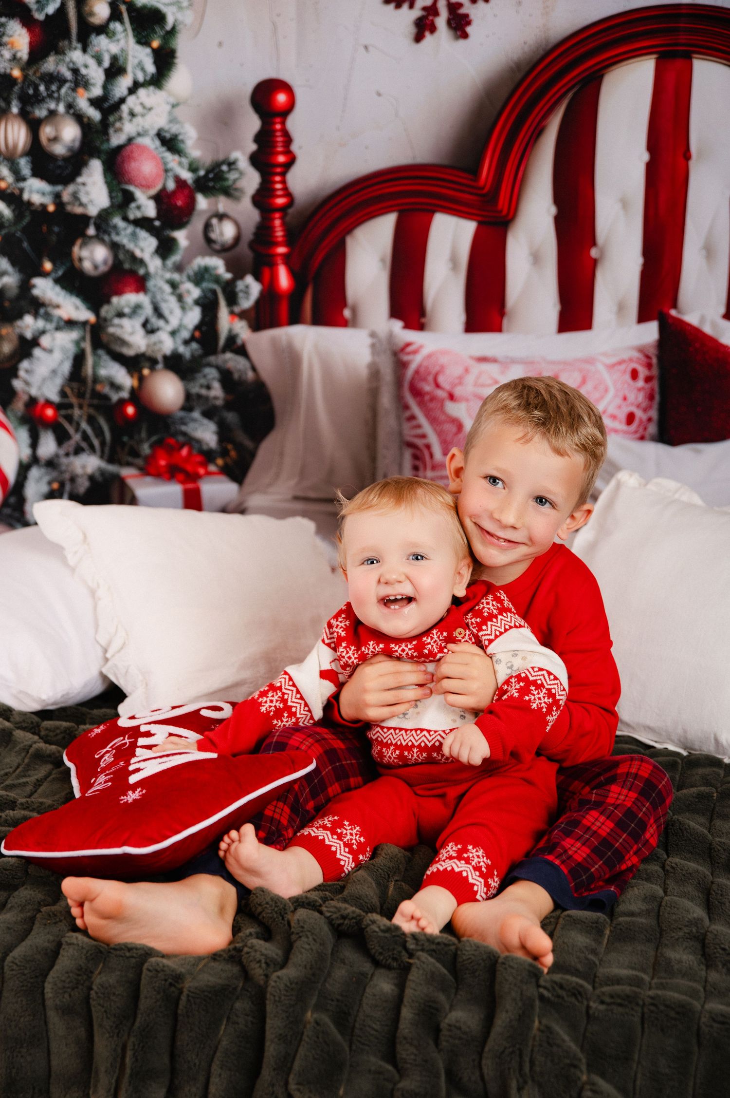 A festive Christmas photo session with two children in red and plaid outfits on a dark green velvet couch.
