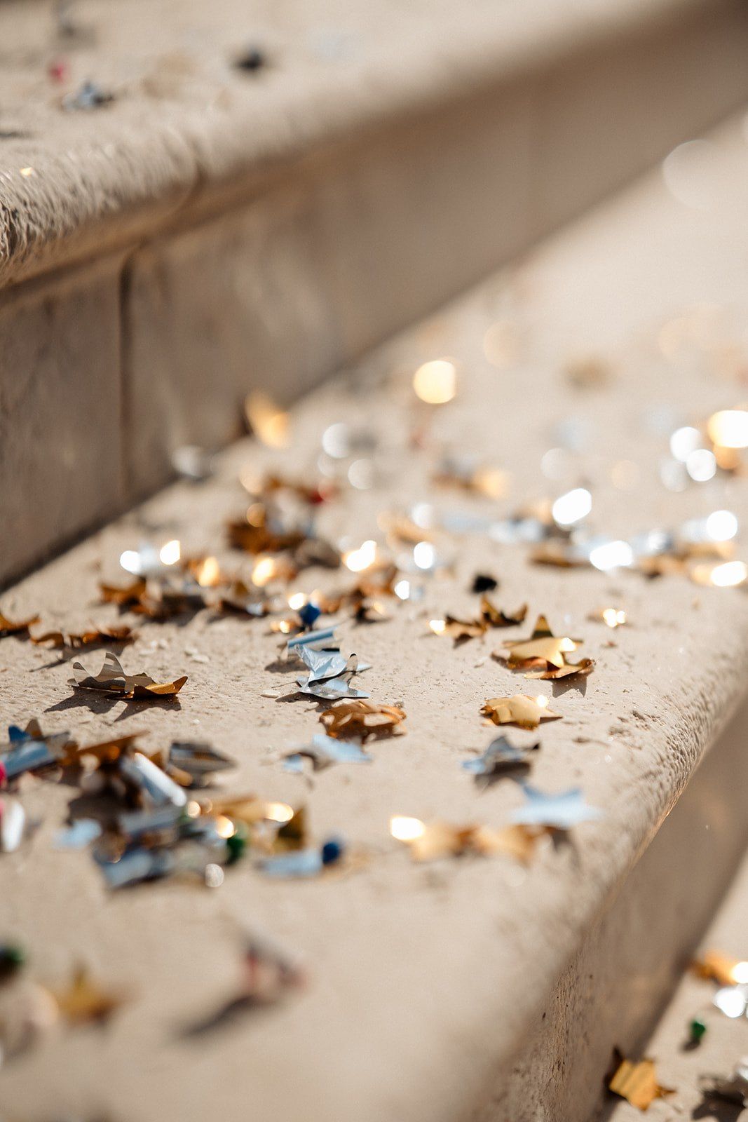 Gold and silver star-shaped confetti scattered on stone steps in warm sunlight.