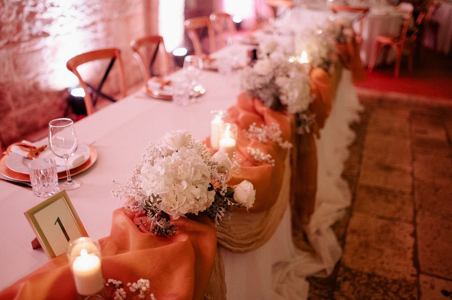 Elegant wedding reception table decorated with orange satin runners, white floral centerpieces, and candles.