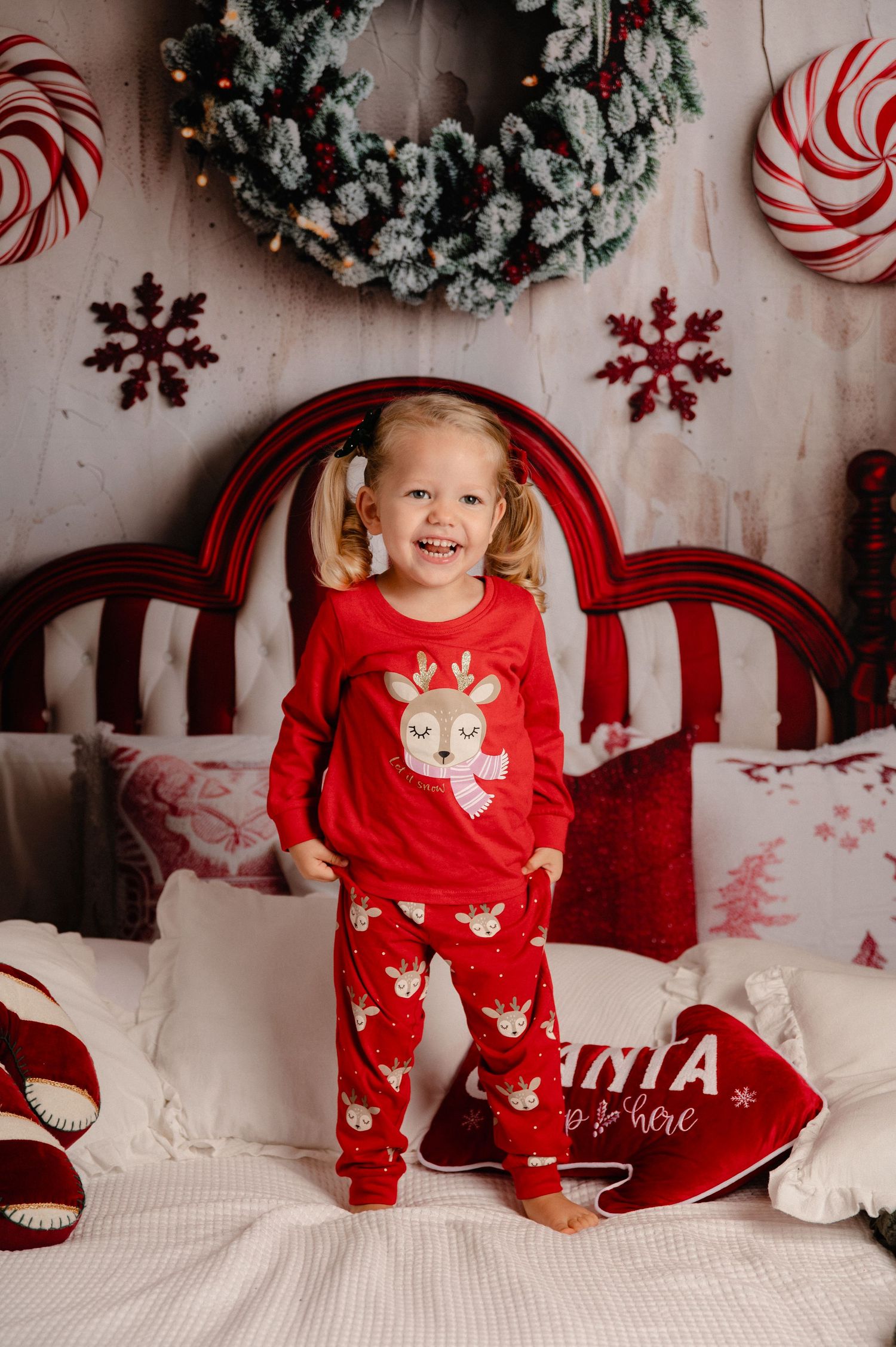 Festive holiday photo session with red and white decor featuring wreaths, candy canes, and snowflakes on white backdrop.
