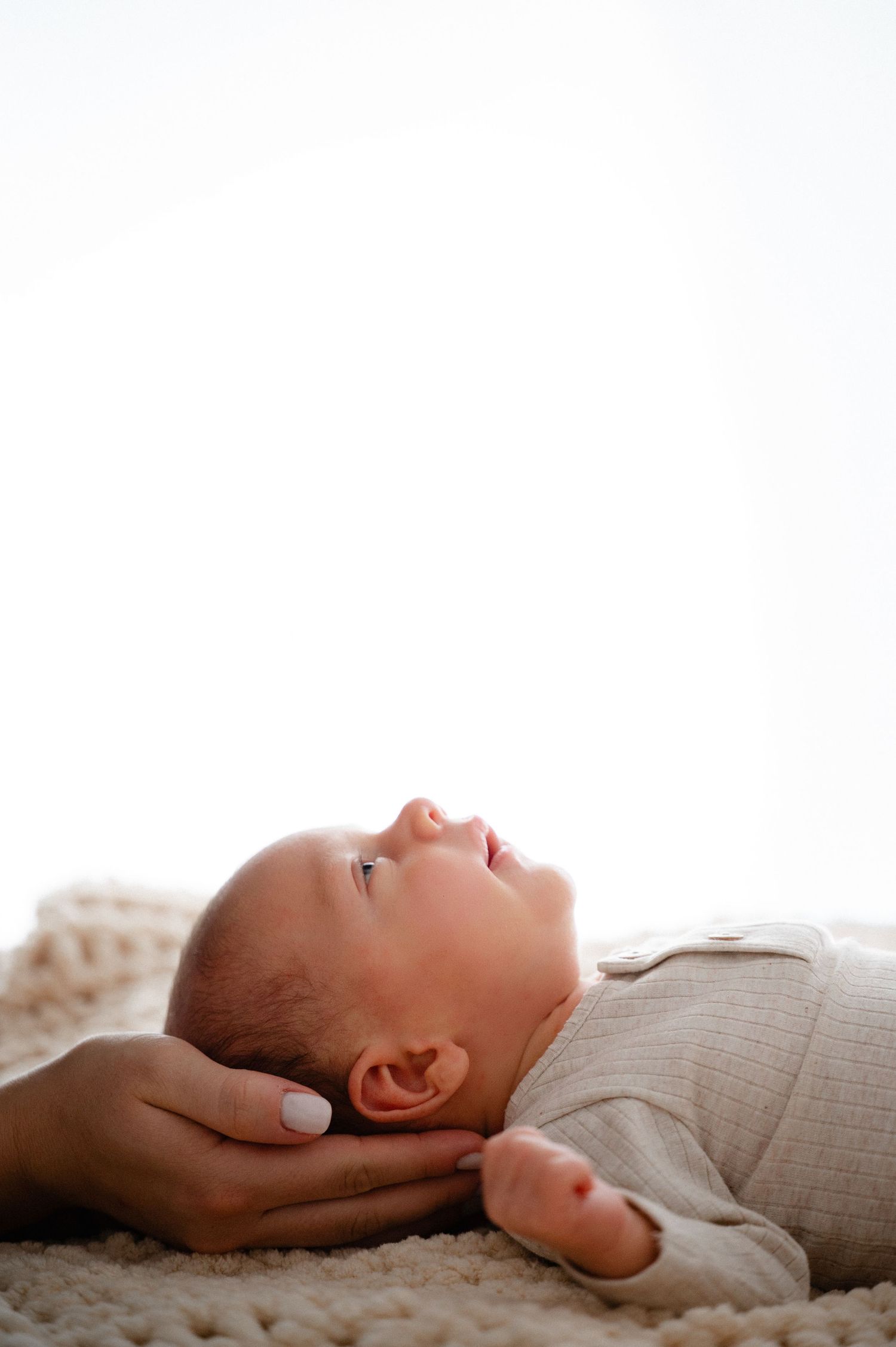 A newborn baby in a white onesie lies peacefully on a soft blanket during a professional photo session.