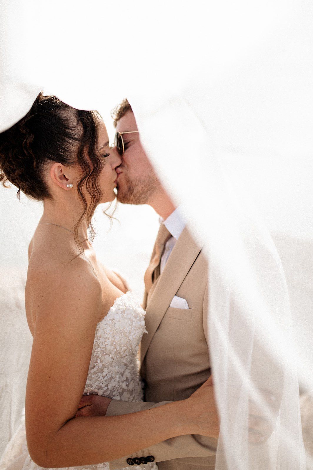 Bride and groom sharing a romantic kiss under a flowing white veil on their wedding day.