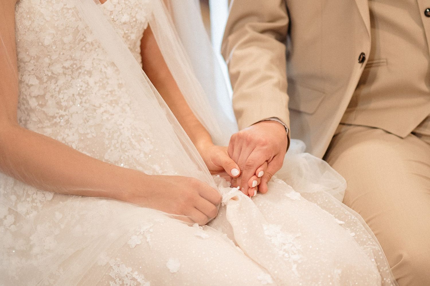 Bride and groom holding hands at wedding ceremony, bride in lace gown, groom in beige suit.