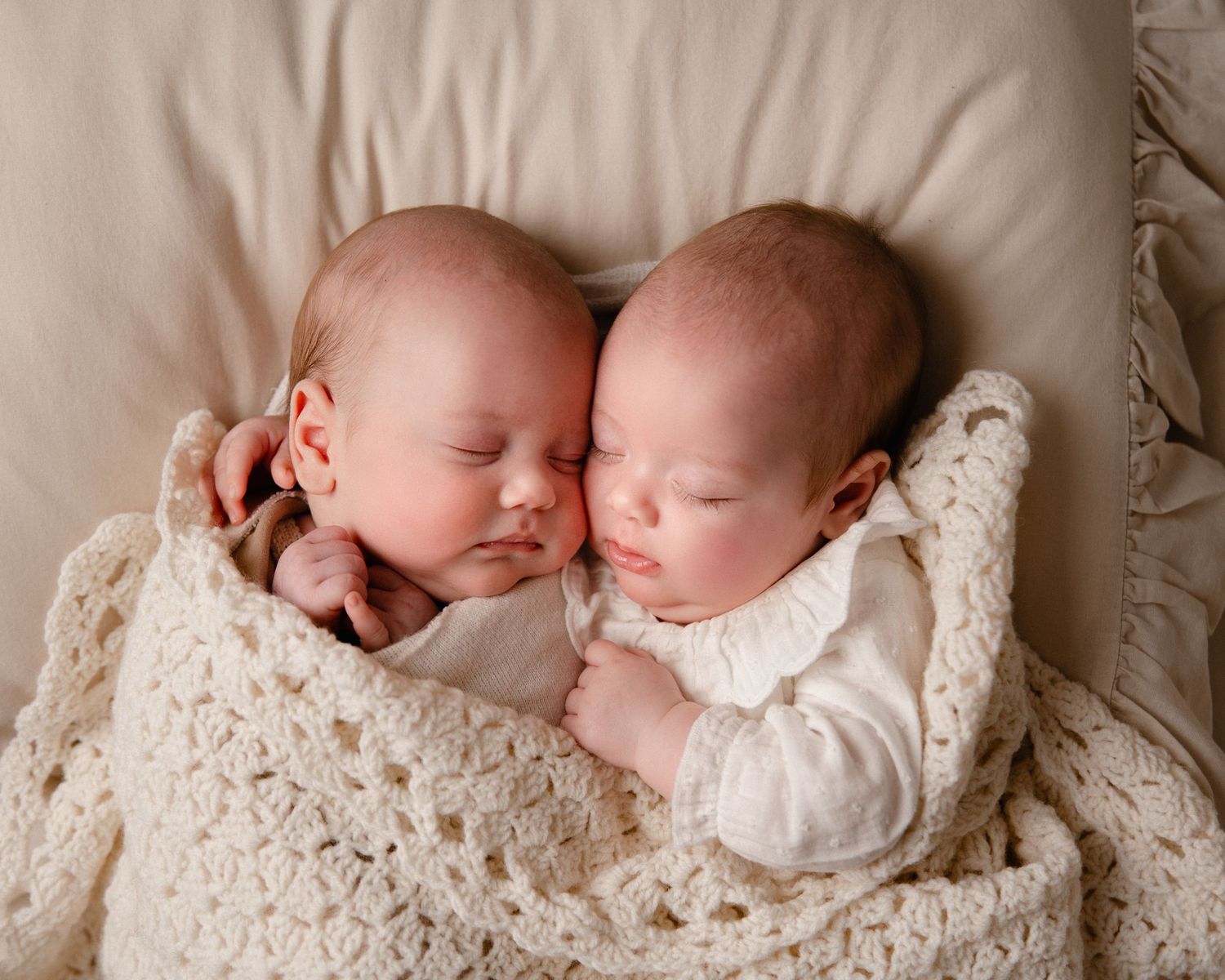 Sleeping newborn twins nestled together on cream-colored blankets in a series of peaceful poses.