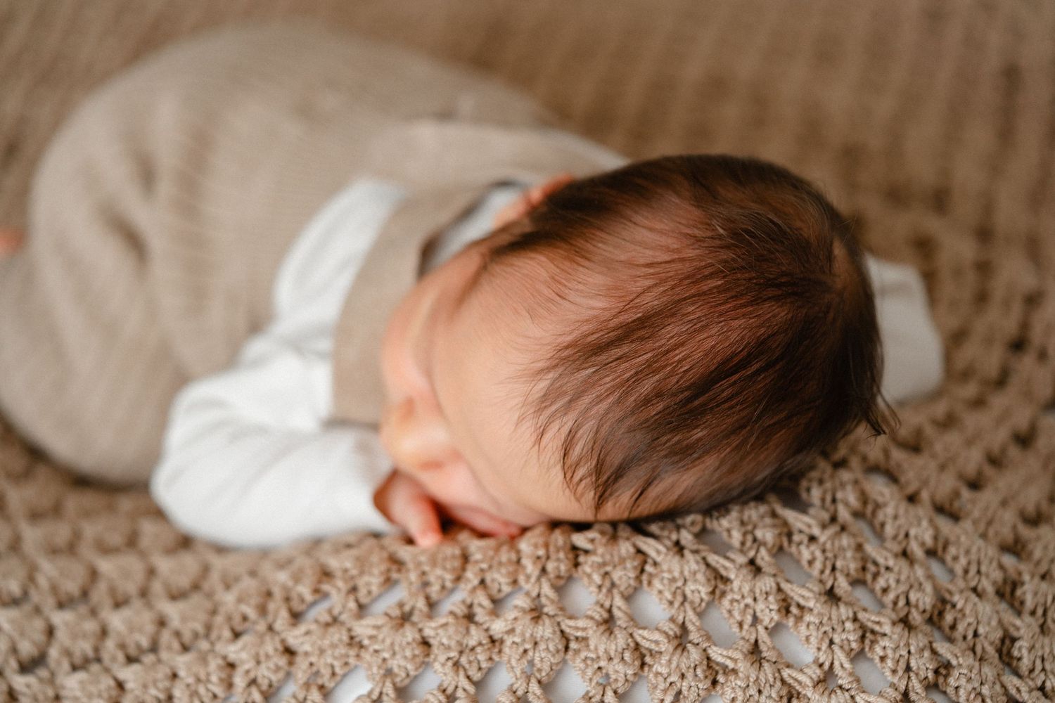 Newborn baby sleeping peacefully on textured beige blanket in natural light.