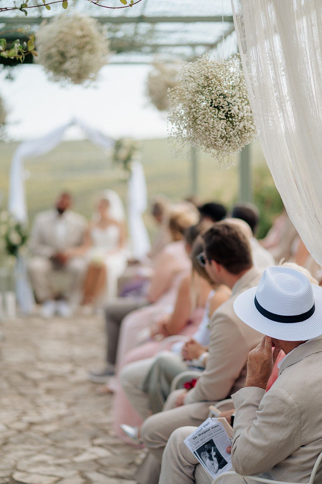 Elegant outdoor wedding ceremony with guests seated under white drapes and baby's breath floral arrangements.