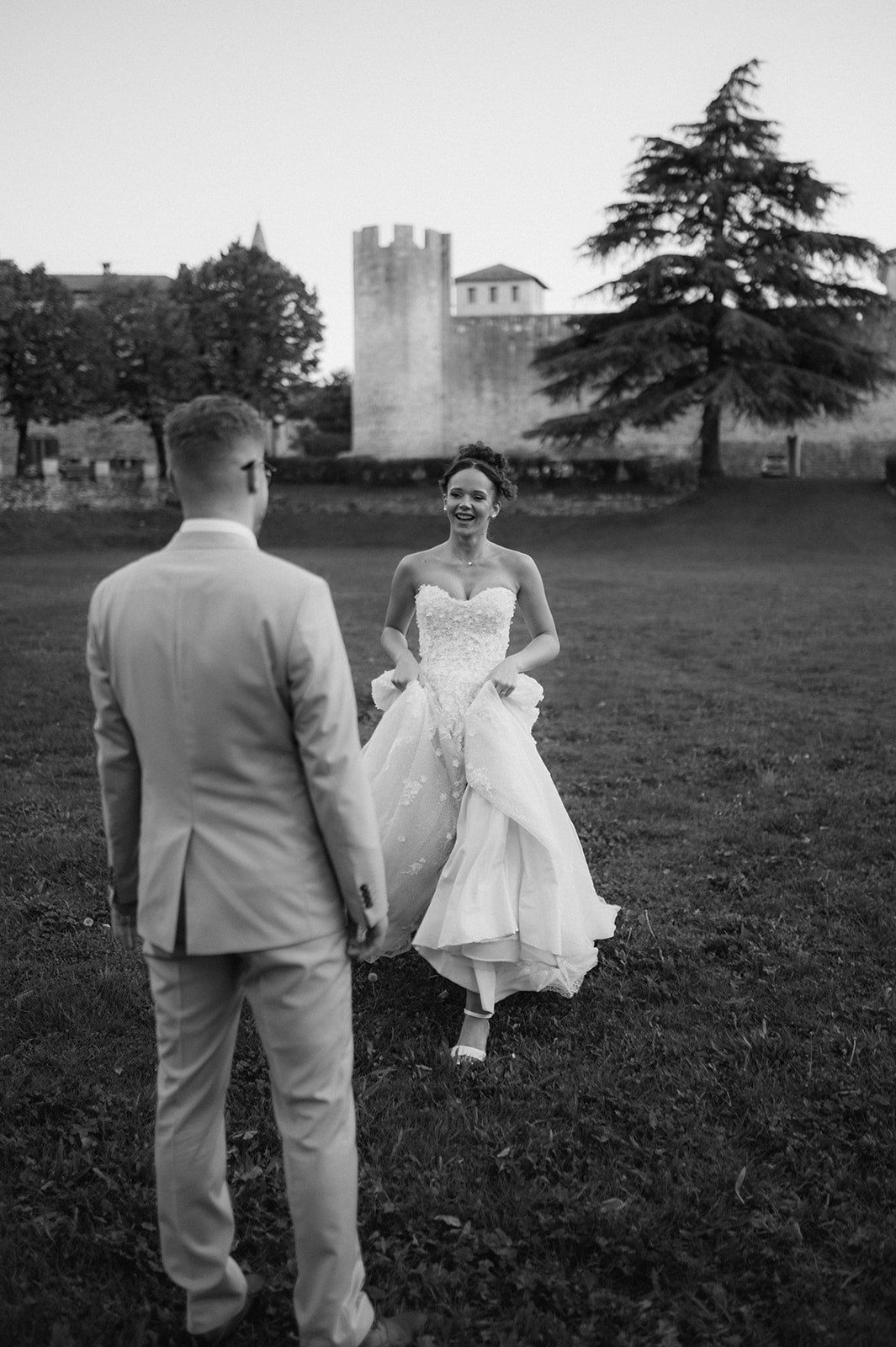 Black and white photo of a bride walking toward groom in a castle garden at dusk.