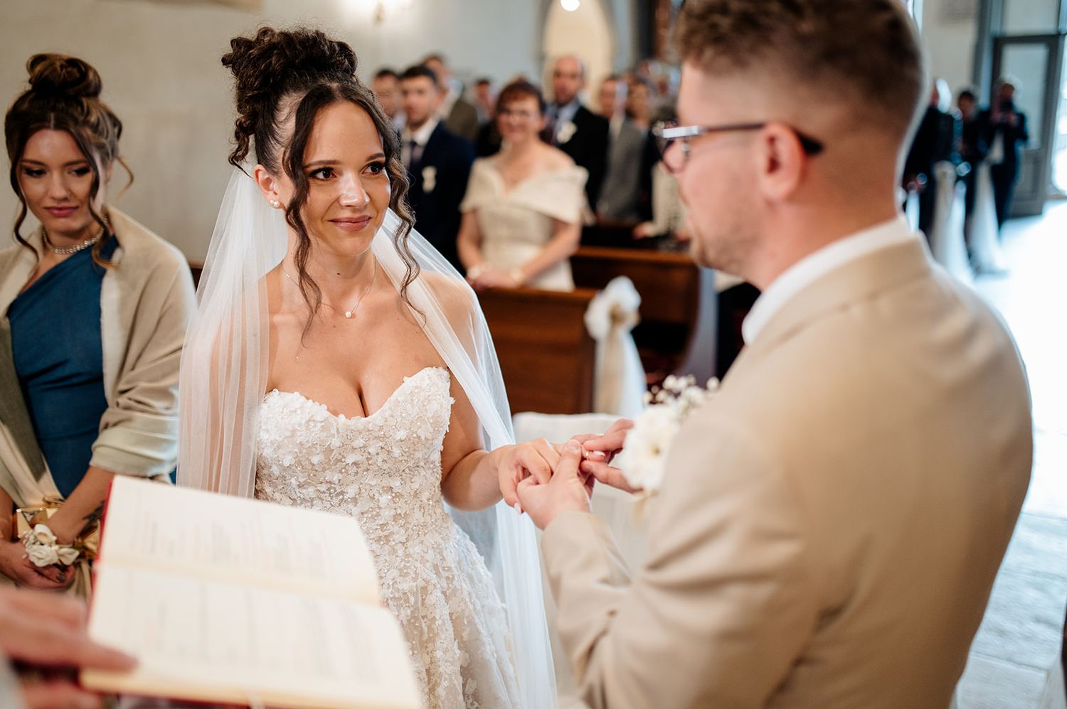 Bride and groom exchanging rings at church altar during wedding ceremony, bride in lace gown smiling.