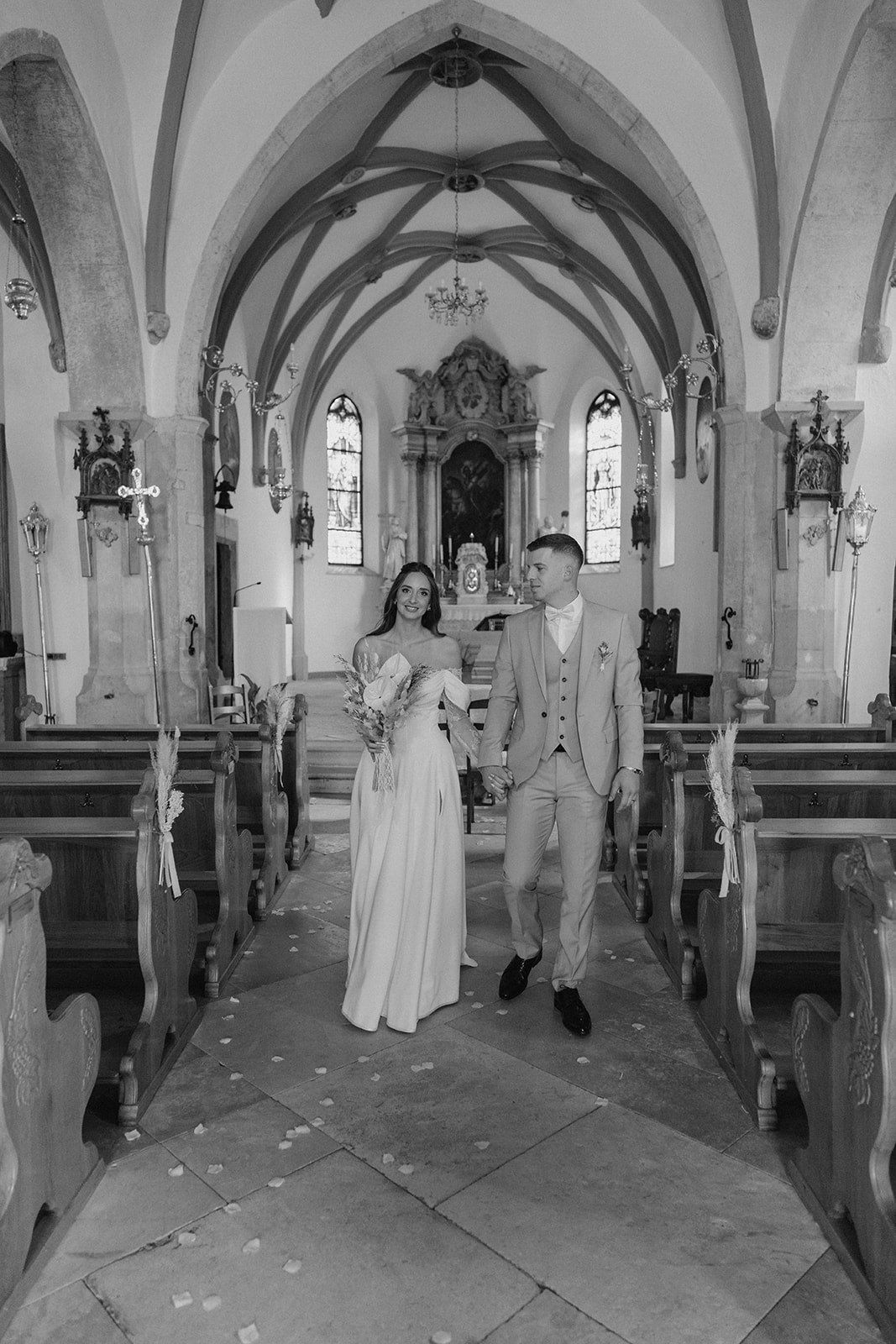 Black and white photo of a bride and groom walking down the aisle of a historic church after their wedding ceremony.