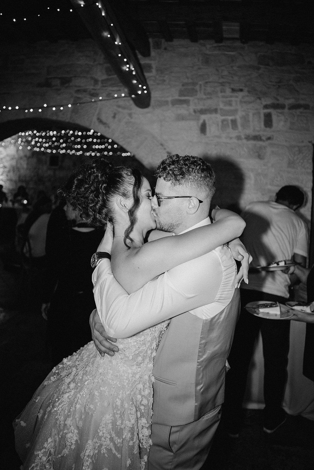 Black and white photo of a bride and groom sharing a romantic kiss during their wedding reception.